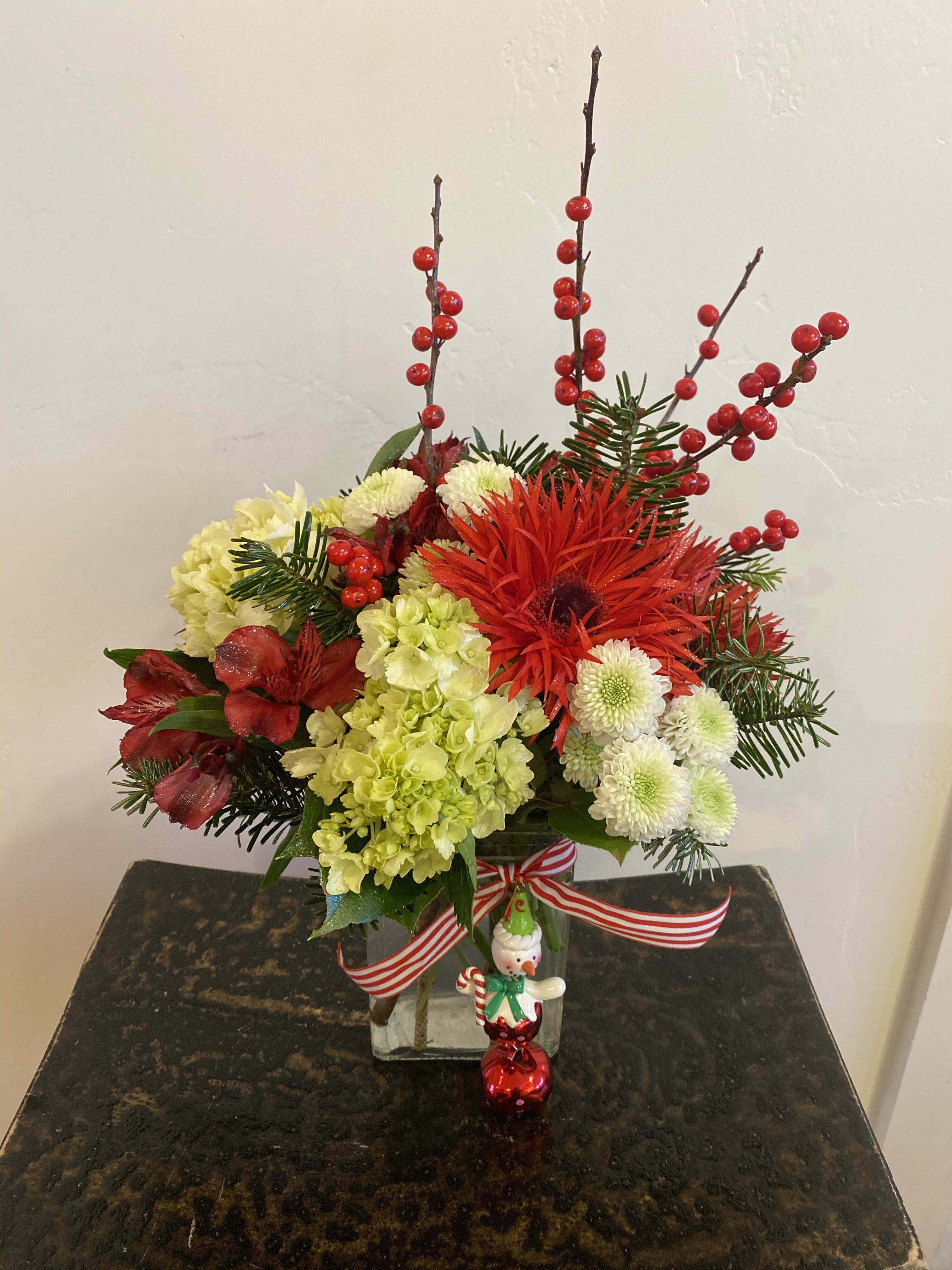 Simply Christmas  - An arrangement Designed in a clear rectangular glass vessel. Filled with fresh green hydrangea, red alstroemeria, red Gerbera daisies, button poms, fragrant evergreens and Ilex berry stems. Tied off with a festive ribbon. (ornament not included)