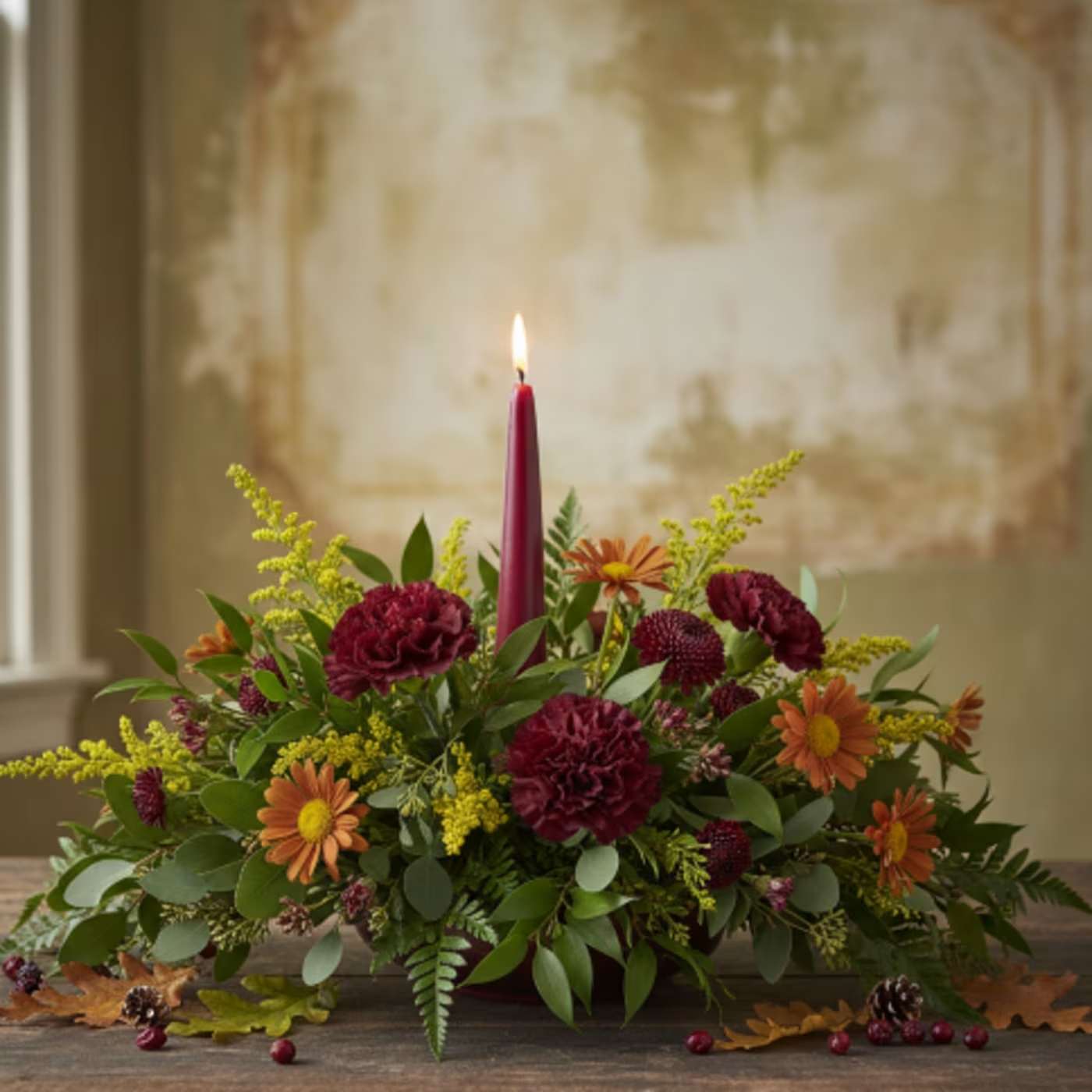 Holiday Centerpiece - As we express our gratitude, we must never forget that the highest appreciation is not to utter words but to live by them.” – John F. Kennedy  Bring the vibrant, natural beauty of the Rockies to your holiday table with our locally-inspired Colorado Autumn Centerpiece. This unique arrangement perfectly captures the spirit of the season with a blend of elegant blooms and rustic, foraged elements.  This festive design features a classic burgundy candle at its heart, surrounded by a rich mix of textures and colors. The florals include: Rich burgundy carnations and cremones, adding depth and warmth. Rust-colored daisies for a touch of natural, autumnal charm. Bright yellow solidago, offering a sunny contrast that evokes the changing aspen leaves.  This centerpiece is perfect for your Thanksgiving dinner table, a cozy fall gathering, or as elegant seasonal décor. Each arrangement is a one-of-a-kind, handcrafted creation, making it a thoughtful and personal gift for hosts, friends, or family. Its warm, welcoming tones and elegant design are sure to create a memorable atmosphere for your holiday celebration.