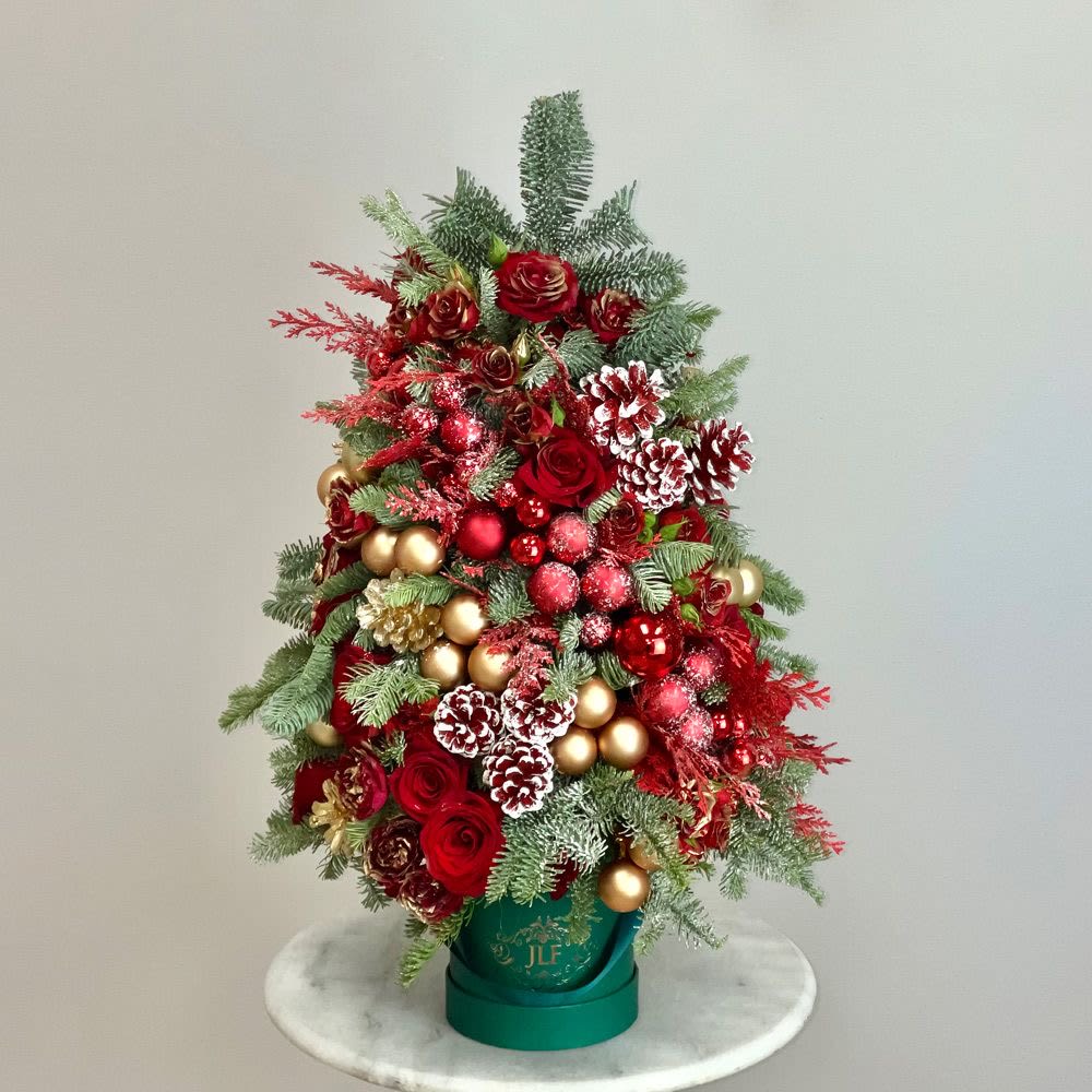 The perfect gift ( Christmas tree floral box) - Elegant floral composition in the shape of a Christmas tree of aromatic natural pine, with red roses, pine flowers, natural, golden and red Christmas spheres in 2 sizes and ambar christmas lights ,assembled in an elegant red or white shiny box . Available every day .