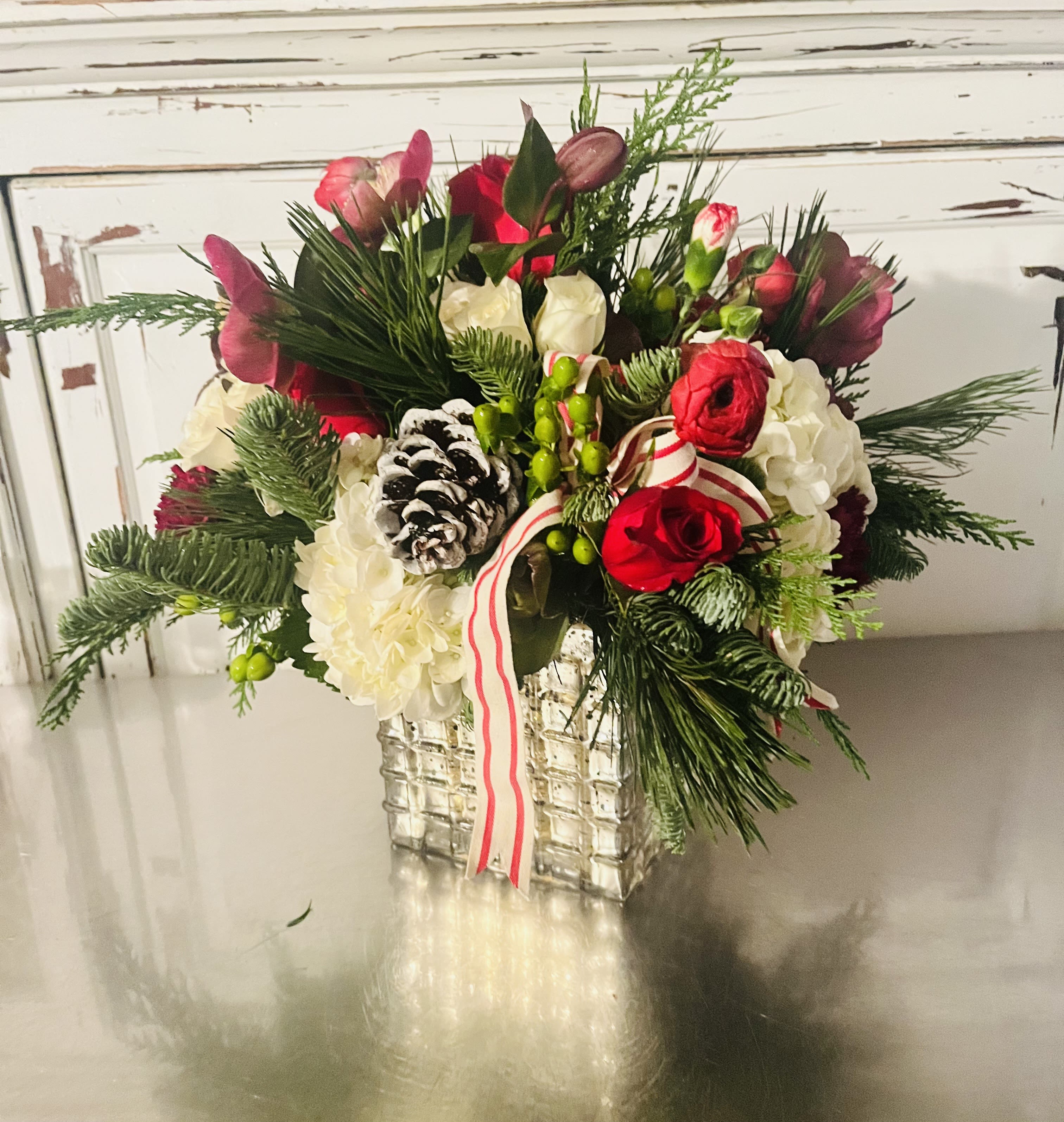 Christmas Flair - This Holiday design is sure to bring Good tidings of comfort and joy this Holiday Season! Designed in a Square, Mercury Glass vessel filled with in season Holiday greens, festive flowers mainly in Red and Whites with added pine cones, berries and a bow to top it off.  