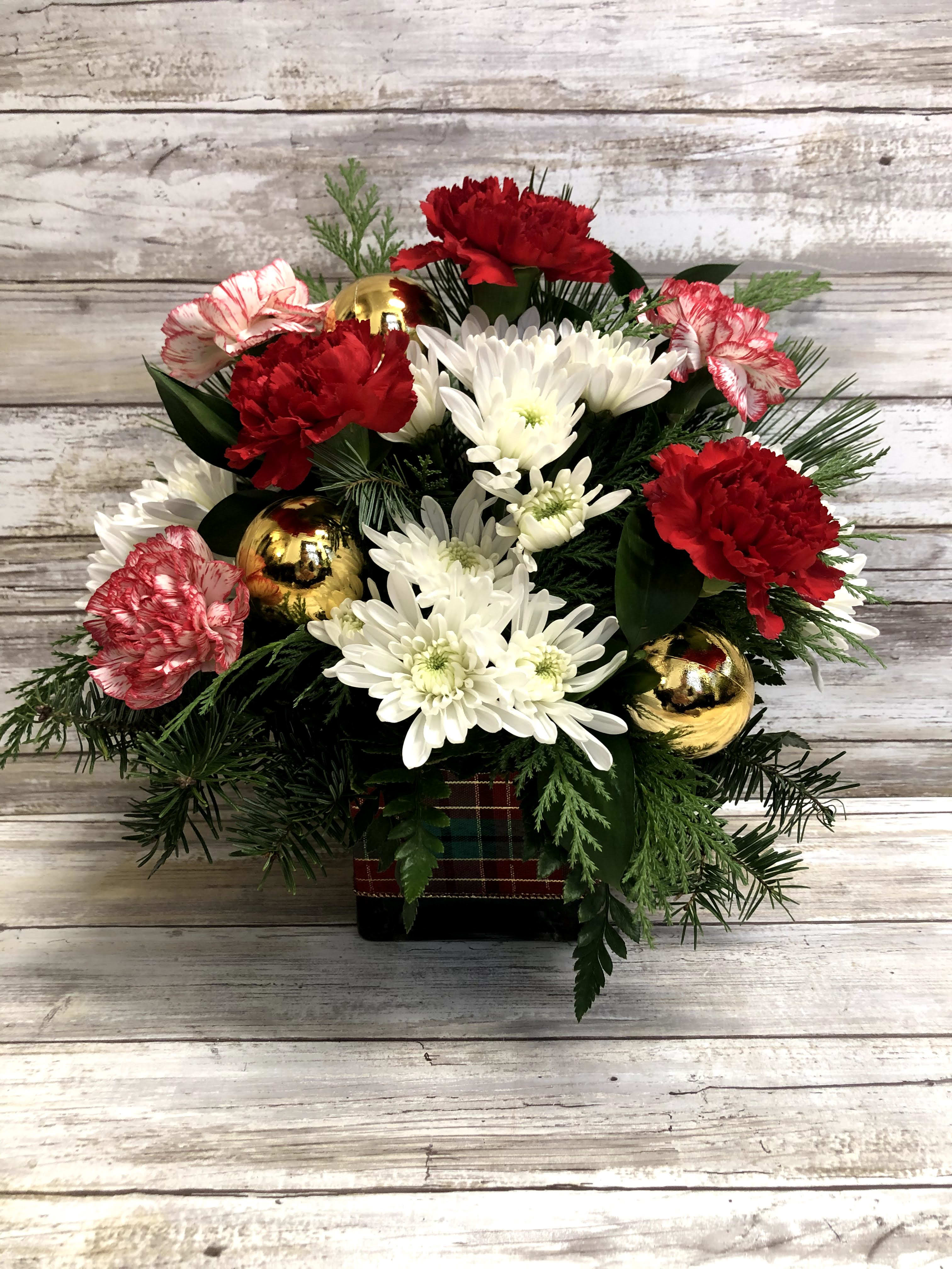 All Wrapped Up - Wrap them in love with this special holiday delivery! Red carnations, white snowflake poms and fresh winter greens and our glass cube wrapped in holiday ribbon make for a festive gift they'll long remember.  Approximately 12&quot; Tall