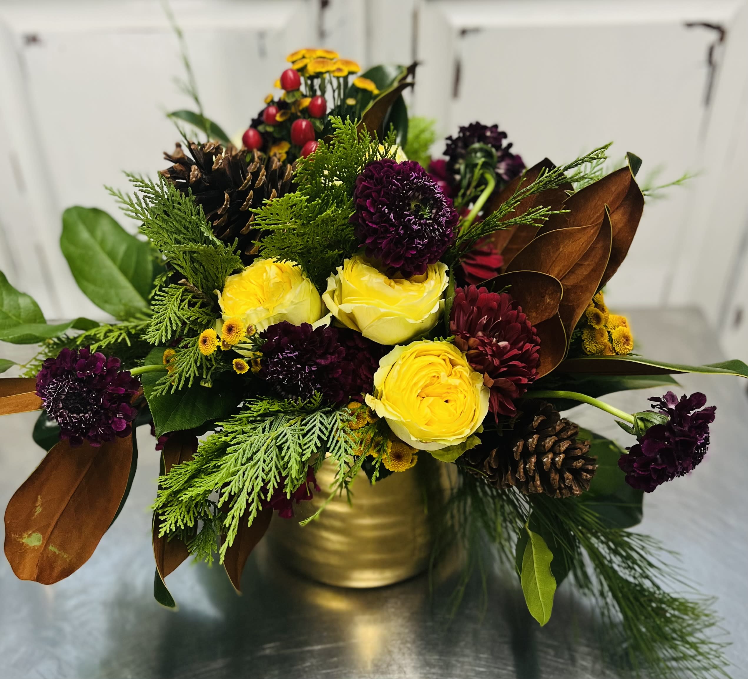 The Crown Jewel - This stunning design is a real JEWEL! Designed in a Gold vessel, Foam Free. Dark jewel tones keeping in holiday elegance with the premium Yellow Garden Roses, Burgundy Scabiosa, and Bordeaux Dianthus, filler mums. Magnolia branches, Salal leaf and a mix of cedar for a wonderful fresh winter fragrance sure to be enjoyed.perfect for the garden lover. This is a seasonal foam free design. please contact us directly if you have any questions or concerns. 707-470-1606