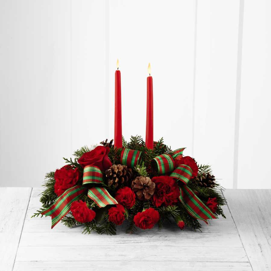 Holiday Cheer Centerpiece - The Holiday Cheer Centerpiece brings rich traditions of Christmas. This festive centerpiece is set to lend its seasonal beauty to your holiday celebrations. Bright red roses, carnations and mini carnations are arranged amongst an assortment of holiday greens, accented with natural pine cones, and 2 red taper candles. This lovely centerpiece will bring warmth and Christmas  charm to your holiday gatherings with each graceful bloom.  B15-4924 
