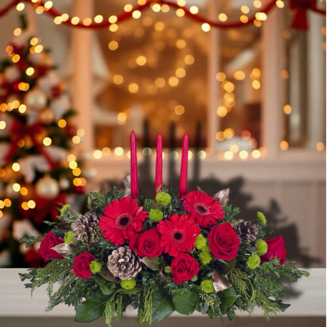 Holiday Glow Candle Centerpiece - Bring warmth and festive elegance to your holiday table with our Holiday Glow Candle Centerpiece. This stunning arrangement features vibrant red roses and cheerful red gerbera daisies, complemented by bright green button mums for a pop of contrast. Lush winter greenery, highlighted with gold-tinted pinecones and foliage, adds seasonal charm and texture. Three classic red taper candles rise gracefully from the center, creating a cozy, inviting glow perfect for Christmas gatherings, dinner parties, or as a heartfelt seasonal gift. Designed to impress from every angle, this centerpiece is a beautiful way to brighten any holiday celebration.