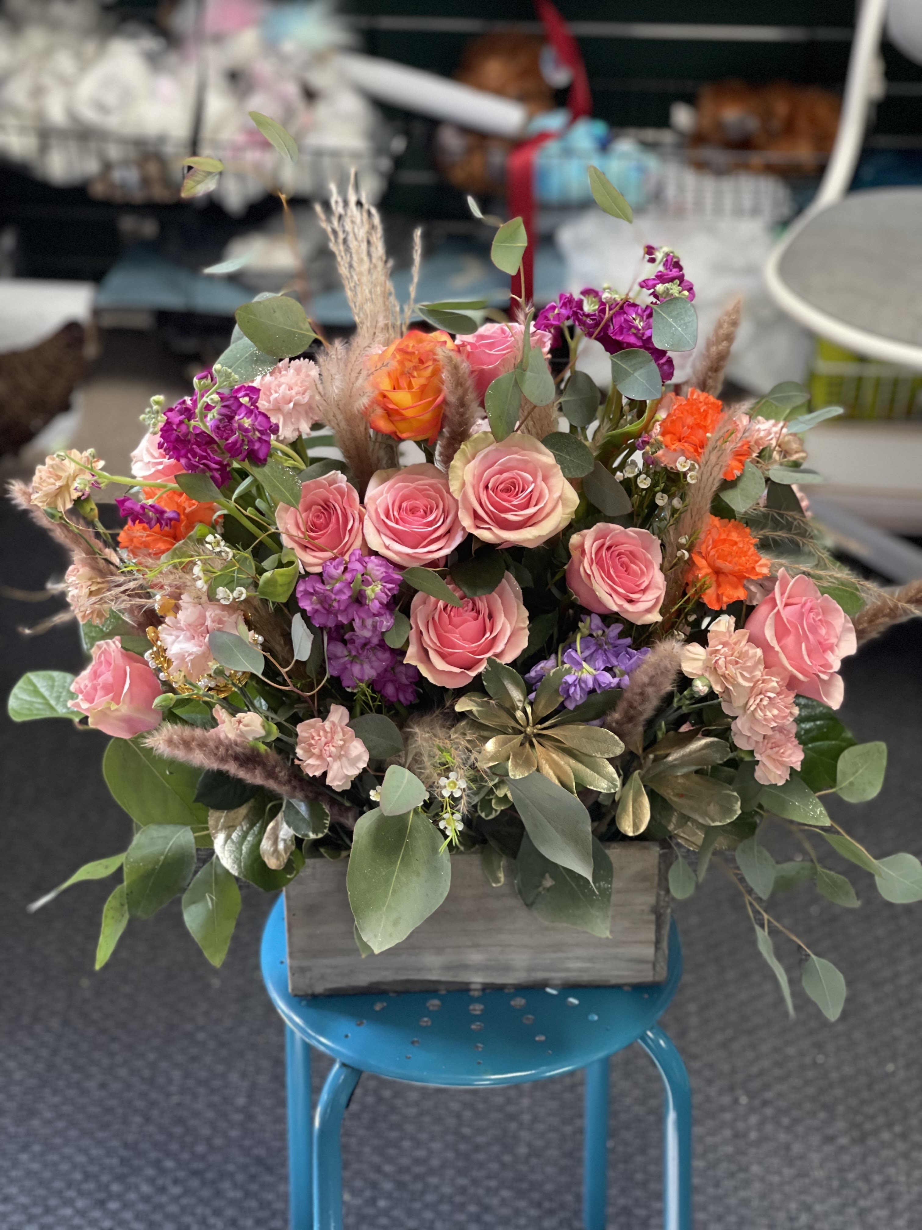 Sunset Serenade  - Let the colors of a perfect sunset bloom in your space with our Sunset Serenade bouquet. This radiant arrangement features a harmonious blend of pink and orange roses, symbolizing admiration and joy, paired with delicate purple accent flowers that add a touch of elegance and mystery. Lush greenery weaves through the vibrant florals, bringing balance and freshness. Artfully presented in a rustic wooden box, this bouquet captures the warmth and romance of a sunset serenade — a beautiful gesture for any occasion. 