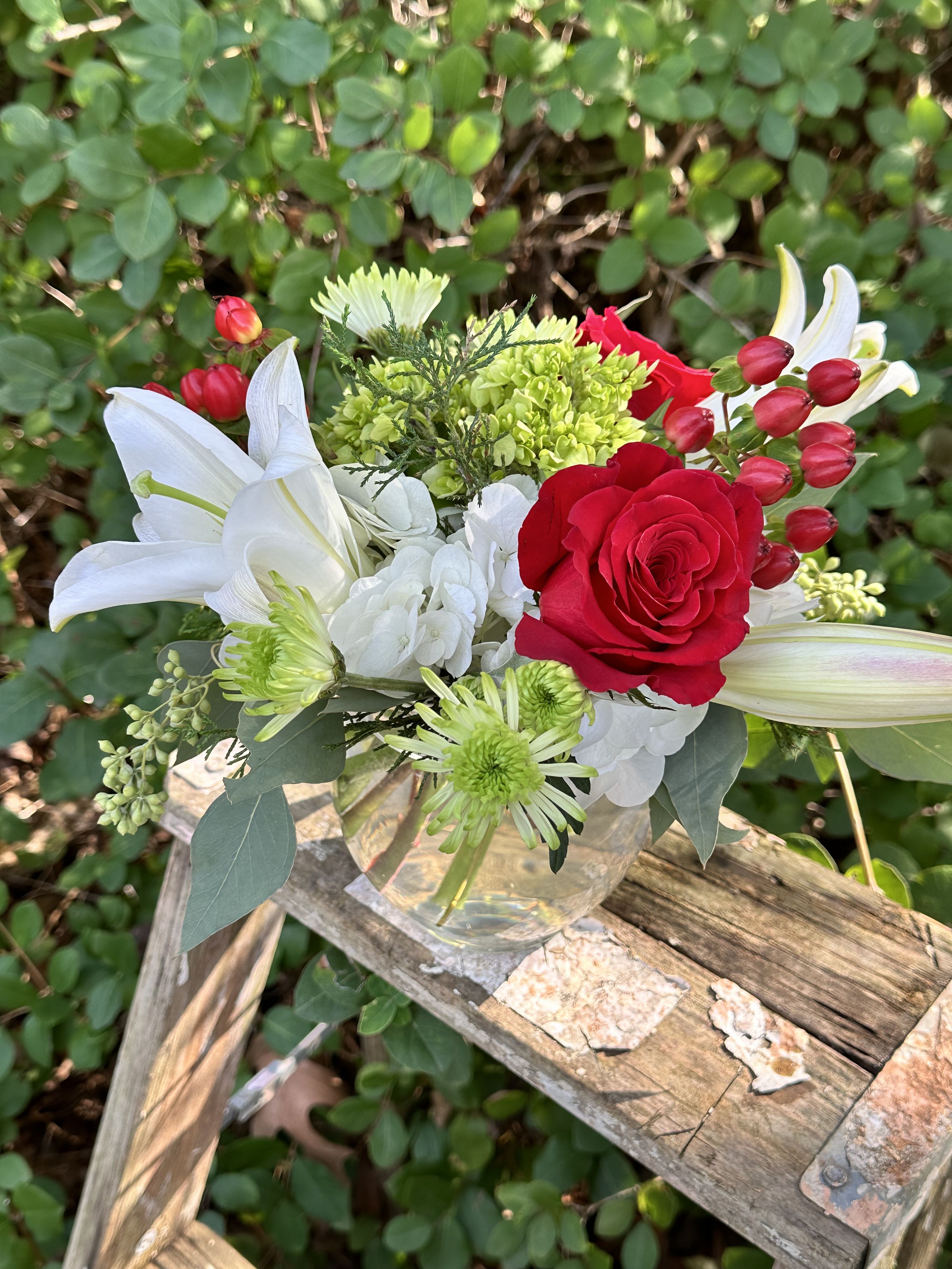 Winter's Whisper - This short, compact arrangement is filled with beautiful white lilies, green chrysanthemums, red roses, red hypericum berries, winter greens, and hydrangeas. Perfect the winter and holiday season!