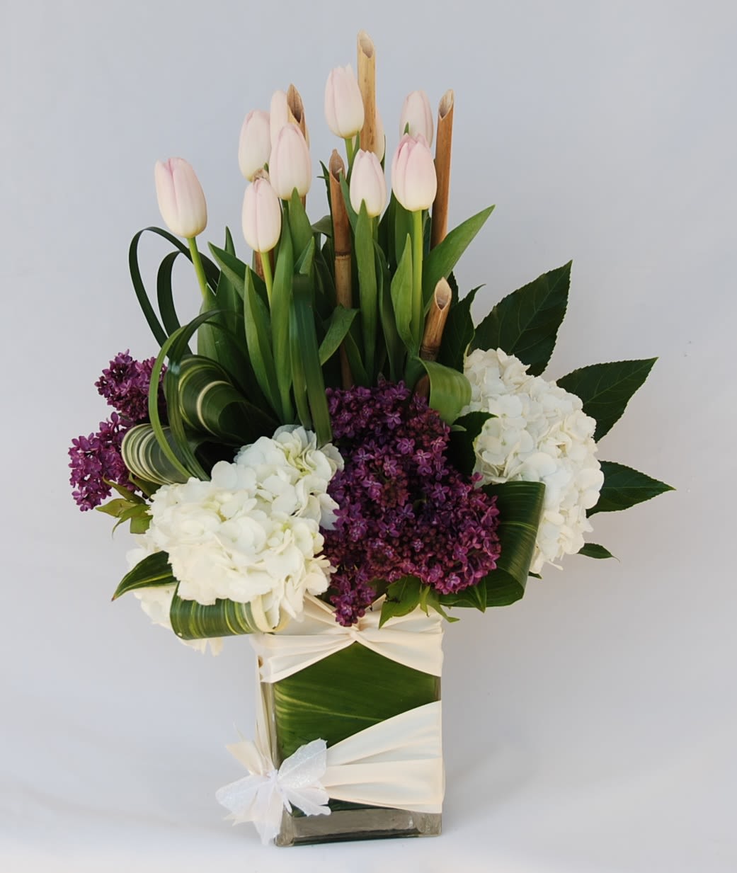 Mother Day Tulips - A rectangular vase filled with hydrangeas, purple lilacs, and tulips,  accented with river cane.