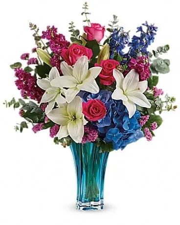 Ocean Dance Bouquet - As enchanting and elegant as the sea, this stunning blown glass vase is the most beautiful shade of azure and features a dramatic swirled shape. What a majestic way to present mom with a fabulous Mother's Day bouquet! Hot pink roses, white asiatic lilies, blue hydrangea, fuchsia stock, blue delphinium, and raspberry sinuata statice are arranged with lemon leaf and spiral eucalyptus. Delivered in a Heart's Pirouette vase.