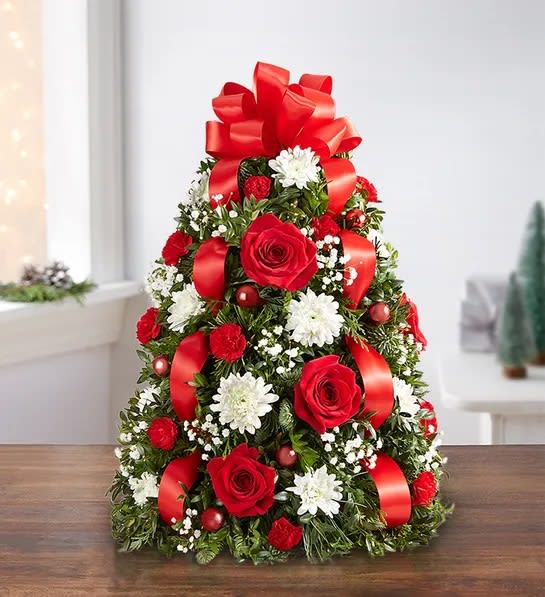 Holiday Flower Tree - The holiday favorite that started it all! Our flower tree arrangement is popular for its festive style and compact size, which fits perfectly into any space. Gathered with fragrant evergreens, then trimmed with decorative ornaments and a merry red bow on top, this floral twist on a traditional tree makes a truly original gift for family, friends or your own home.  - Tree-shaped arrangement with red roses and mini carnations; white cushion poms; accented with baby’s breath, assorted Christmas greenery, red ball ornaments and a red bow topper - Premium arrangement measures approximately 22&quot;H x 16&quot;W - Deluxe arrangement measures approximately 21&quot;H x 13&quot;W - Standard arrangement measures approximately 20&quot;H x 12&quot;W - Our florists hand-design each arrangement, so colors and varieties may vary due to local availability