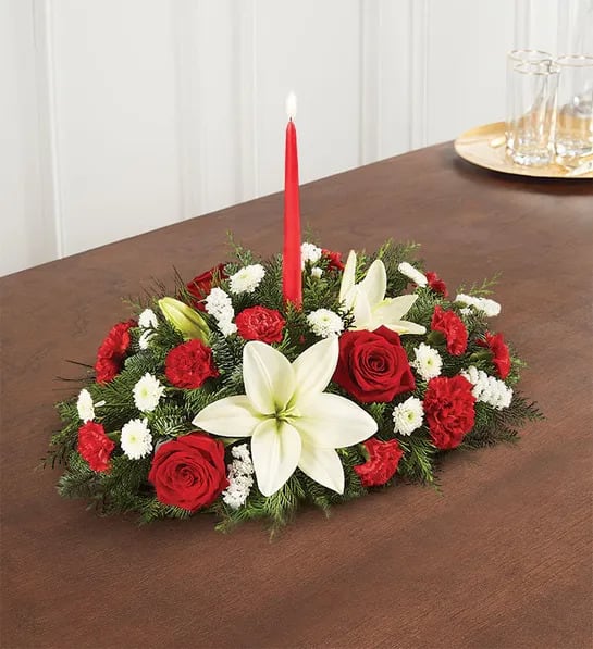 Traditional Christmas Centerpiece - Our traditional table arrangement creates the perfect centerpiece for your Christmas celebration. Beautifully designed with long-lasting blooms in seasonal colors, this fragrant gathering features red taper candles to cast a warm, cozy glow throughout the holidays.  Centerpiece arrangement with red roses, carnations and mini carnations; white Asiatic lilies, button poms and statice; accented with assorted Christmas greenery  Premium arrangement features two 12&quot;H red taper candles; measures approximately 10&quot;H x 19&quot;L Deluxe arrangement features two 12&quot;H red taper candles; measures approximately 9&quot;H x 15&quot;L Standard arrangement features one 12&quot;H red taper candle; measures approximately 8&quot;H x 13&quot;L  Dimensions do not include height of candles  Our florists hand-design each arrangement, so colors, varieties and container may vary due to local availability  To ensure lasting beauty, Asiatic lilies may arrive in bud form and will fully bloom over the next few days