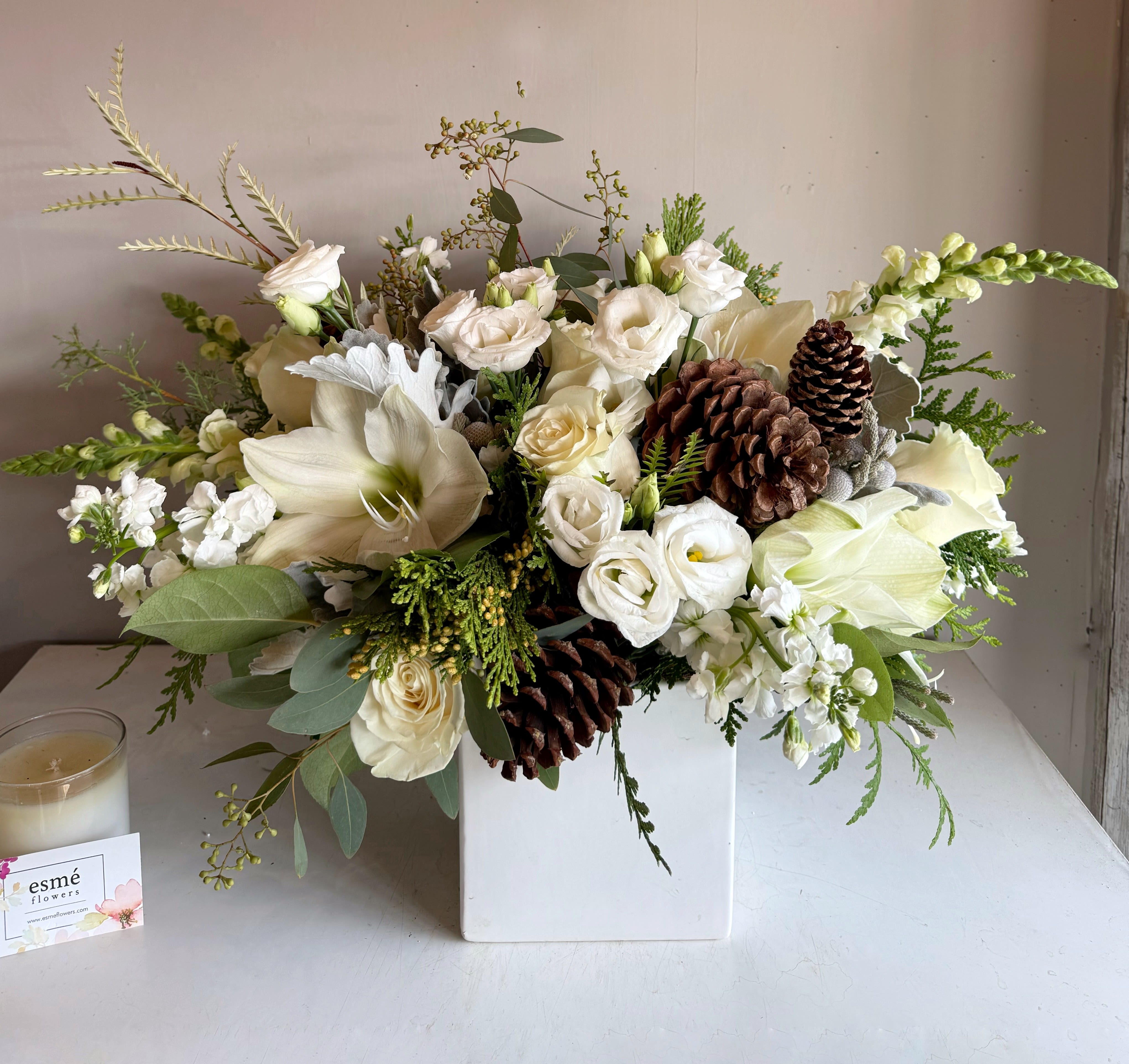 Snowy Wonder - Gorgeous white Amaryllis, lisianthus, Playa Blanca roses, and lush winter evegreens and pinecones in a white ceramic vase. Here's a beautiful winter arrangement to celebrate any occasion!  AVAILABLE 12/6 - 12/31