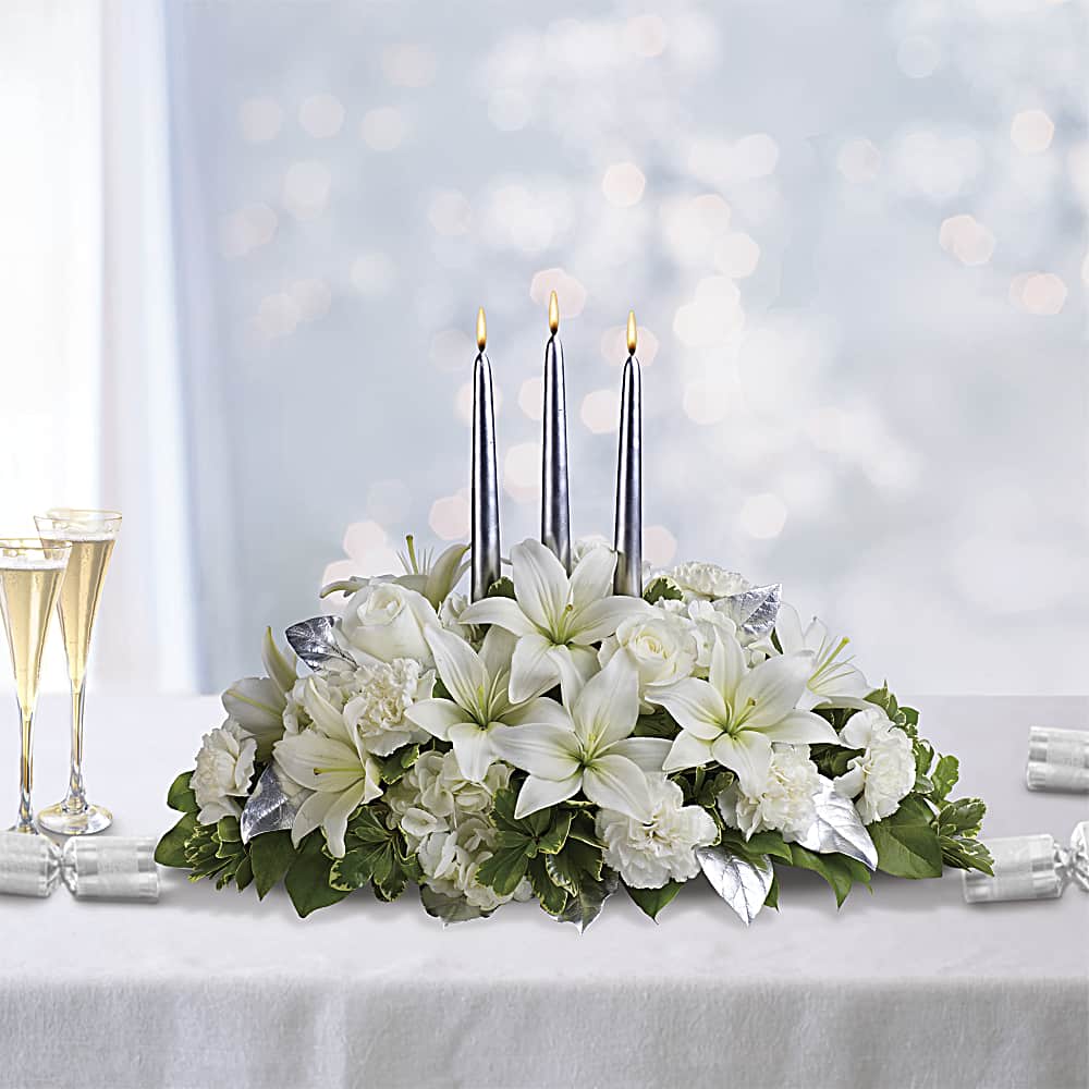 Silver Elegance Centerpiece (DB) - Welcome the arrival of the New Year with a stunning all-white centerpiece that exudes elegance, purity, and fresh beginnings. Our white floral arrangement is carefully handcrafted using a combination of roses, lilies, carnations, and hydrangea, creating a simple yet breathtaking display. The all-white color palette of this centerpiece not only exudes sophistication but also serves as a blank canvas for creativity and personalization.