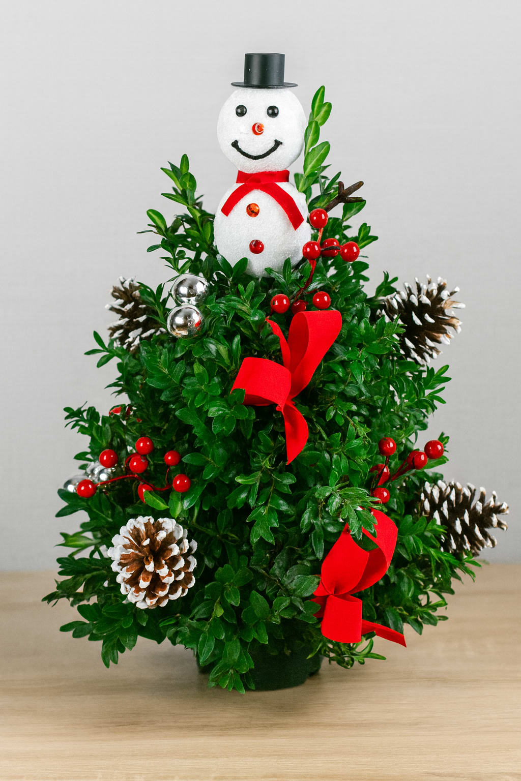Snowman Boxwood Tree  - This classically decorated 16” boxwood tree is handcrafted and topped with a jolly snowman to bring cheer this holiday season! 