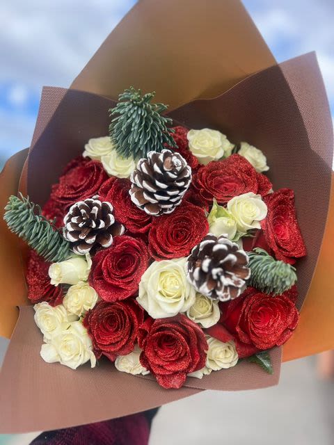Winter Radiance - A dazzling bouquet of red glittered roses, creamy white blooms, frosted pinecones and sprigs of green. Perfect for bringing warmth and elegance to holiday celebrations.