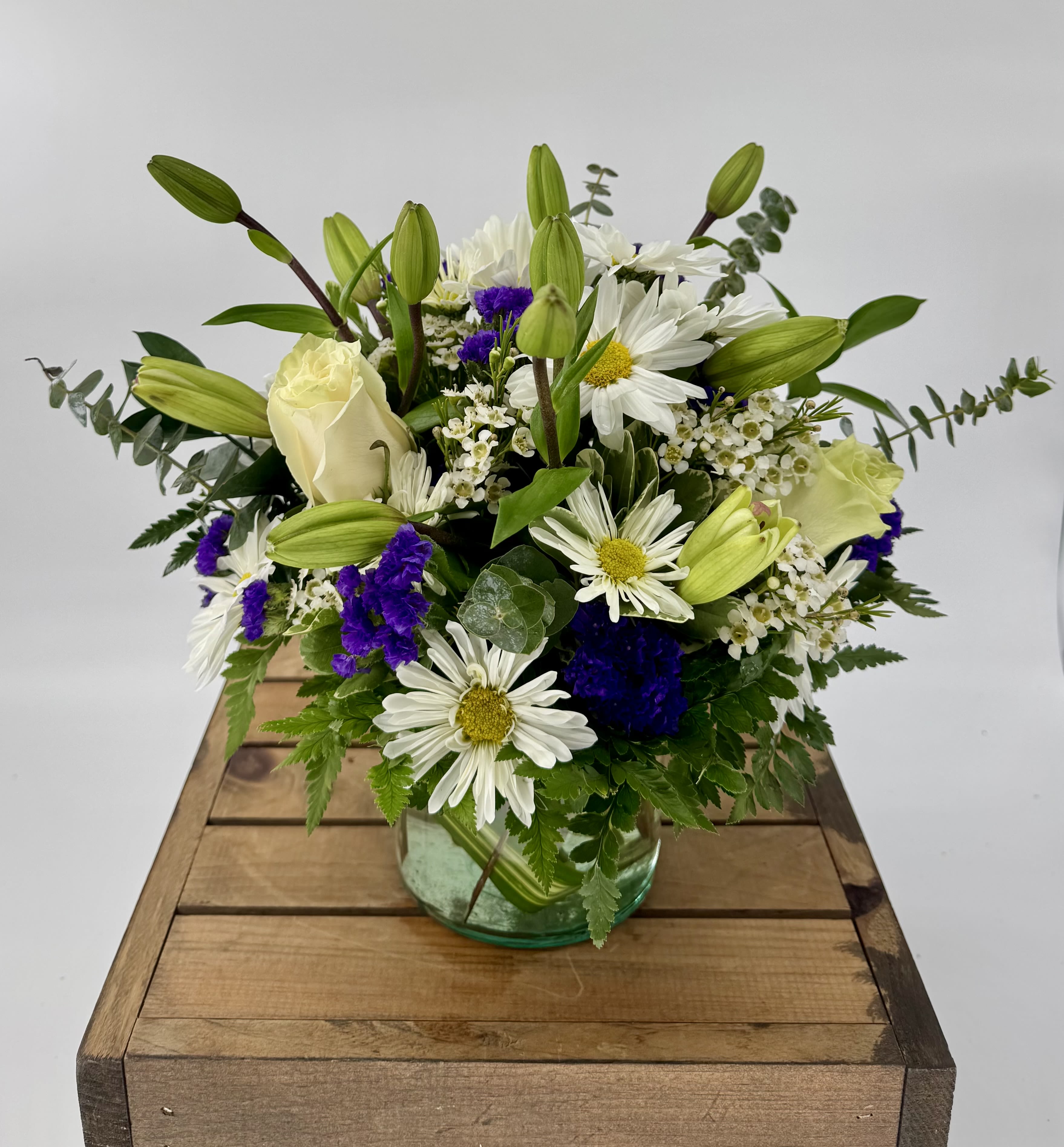 Azure Dream (BR) - Capture the essence of elegance with our exquisite floral arrangement in a clear glass vase. This stunning ensemble showcases the timeless beauty of white lilies, white roses, waxflower and daisies, complemented by the delicate hues of blue statice.