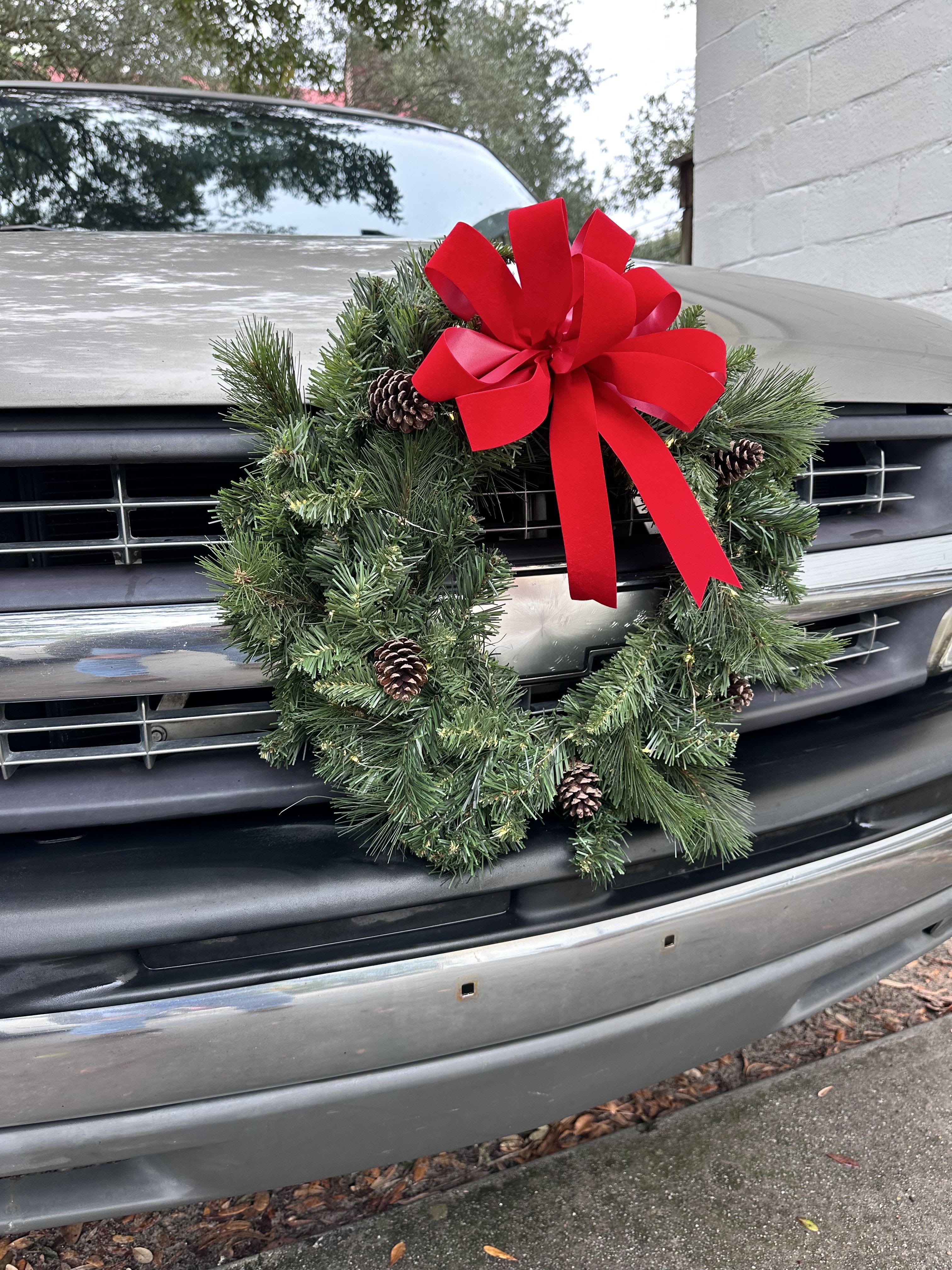 Cruisin’ Christmas Wreath - This festive car wreath brings instant holiday cheer to your drive, featuring lush evergreen tips, natural pinecones, and a bold red holiday bow. Designed to attach securely to the front grille, it’s the perfect way to spread Christmas spirit wherever the season takes you.