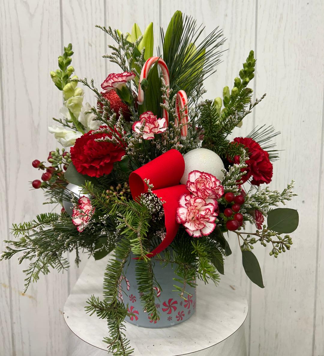 Peppermint Dream Arrangement - Celebrate the season with this festive arrangement of holiday classic flowers &amp; Christmas greens. Accented in a peppermint-themed container and candy canes. Please note: Based on current inventory, some flowers may be substituted. Rest assured, the overall look, feel, and value of the arrangement will be thoughtfully maintained. Approximately 13 inches tall.