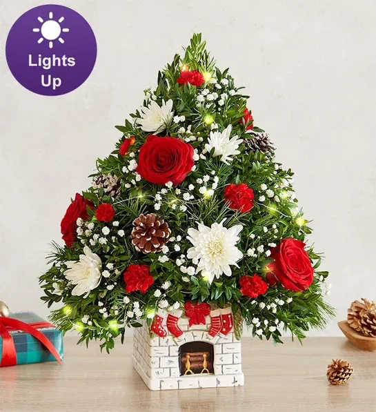 Holiday Flower Tree® Merry Mantel - The joy of gift-giving comes alive in the latest edition of our iconic Holiday Flower Tree, trimmed in festive blooms. It’s designed in our exclusive “The Stockings were Hung Mantel”, which captures the anticipation of Santa’s arrival. This white ceramic container is decorated with four stockings, an evergreen garland and a festive red bow. Complete with white-tipped pinecones and a warm white fairy lights, it’s a magical collectible for the holiday season.