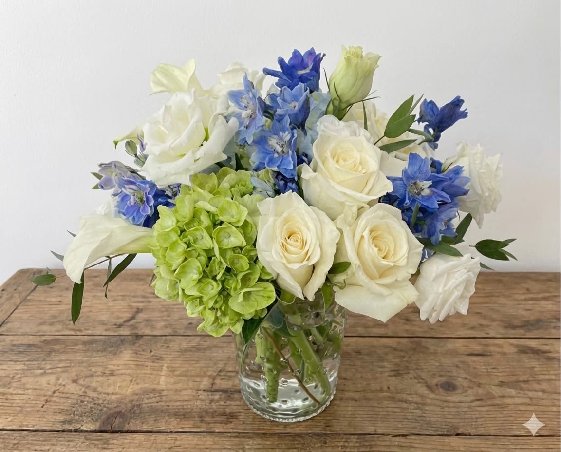 Annie - This arrangement stays in white and blue color. It includes white roses, light blue hydrangea, white calla lily, white lisanthus and blue delphinium. 