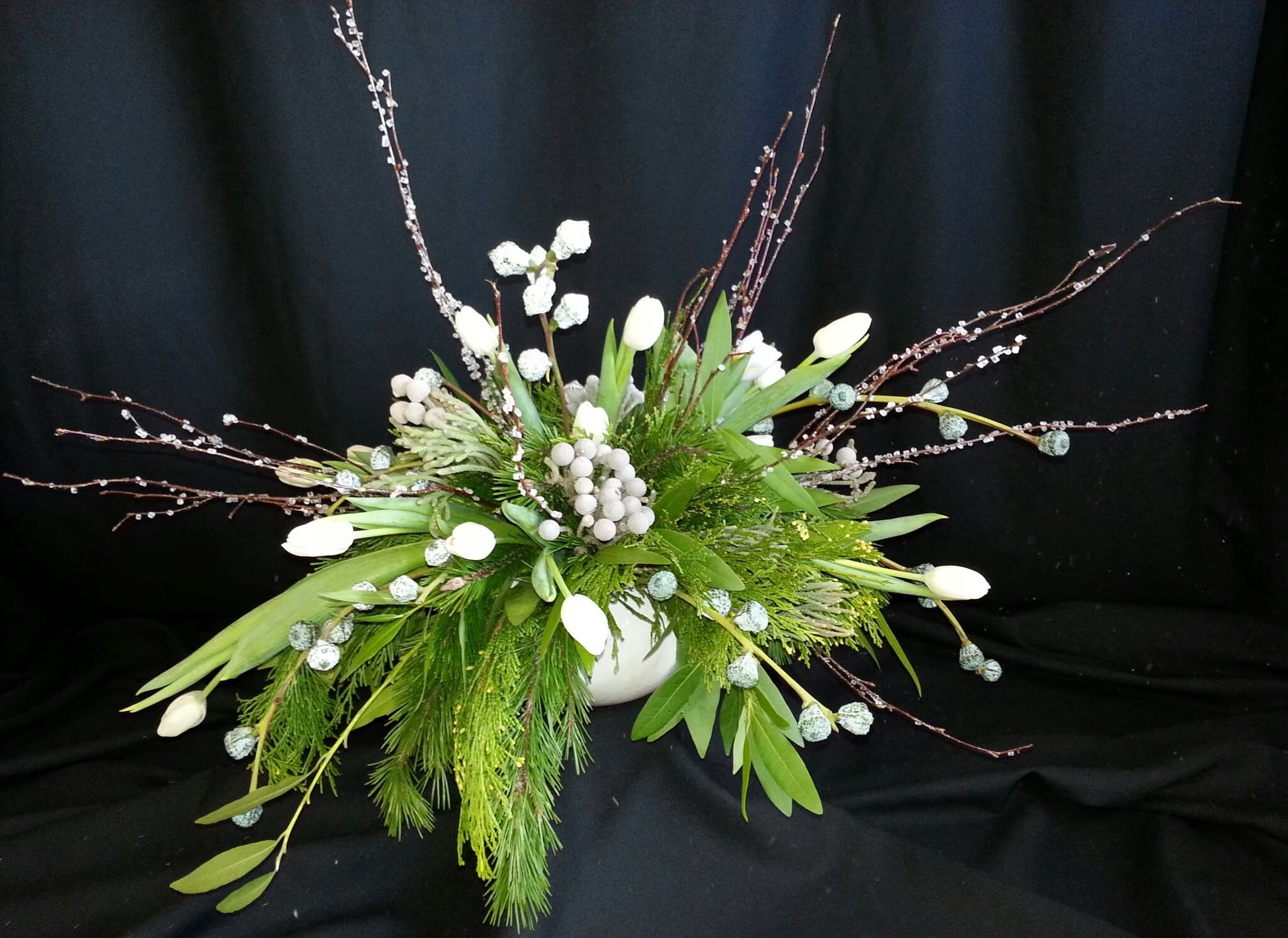 Winter Wonderland Oblong Centerpiece with Branches - Premium silver / blue accents and all white winter flowers create the perfect fantasy Winter Wonderland. We've added sparkling branches and evergreen foliage. Nice addition to your coffee table or credenza for the holiday party!  