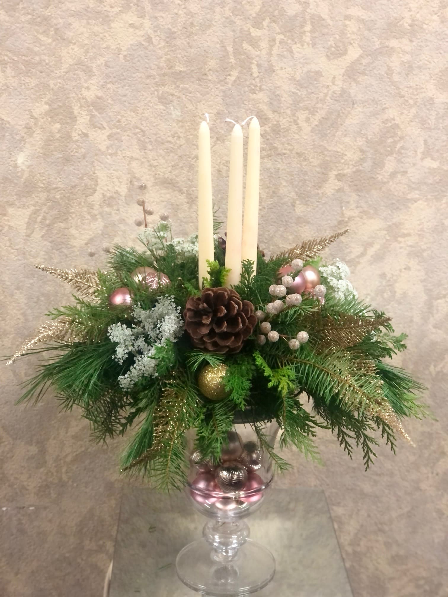 Pink Pine Holiday Centerpiece - Type of Flowers: Pine centerpiece with pink ornaments and gold silks in a tall, crystal vase with pink ornaments and candles.