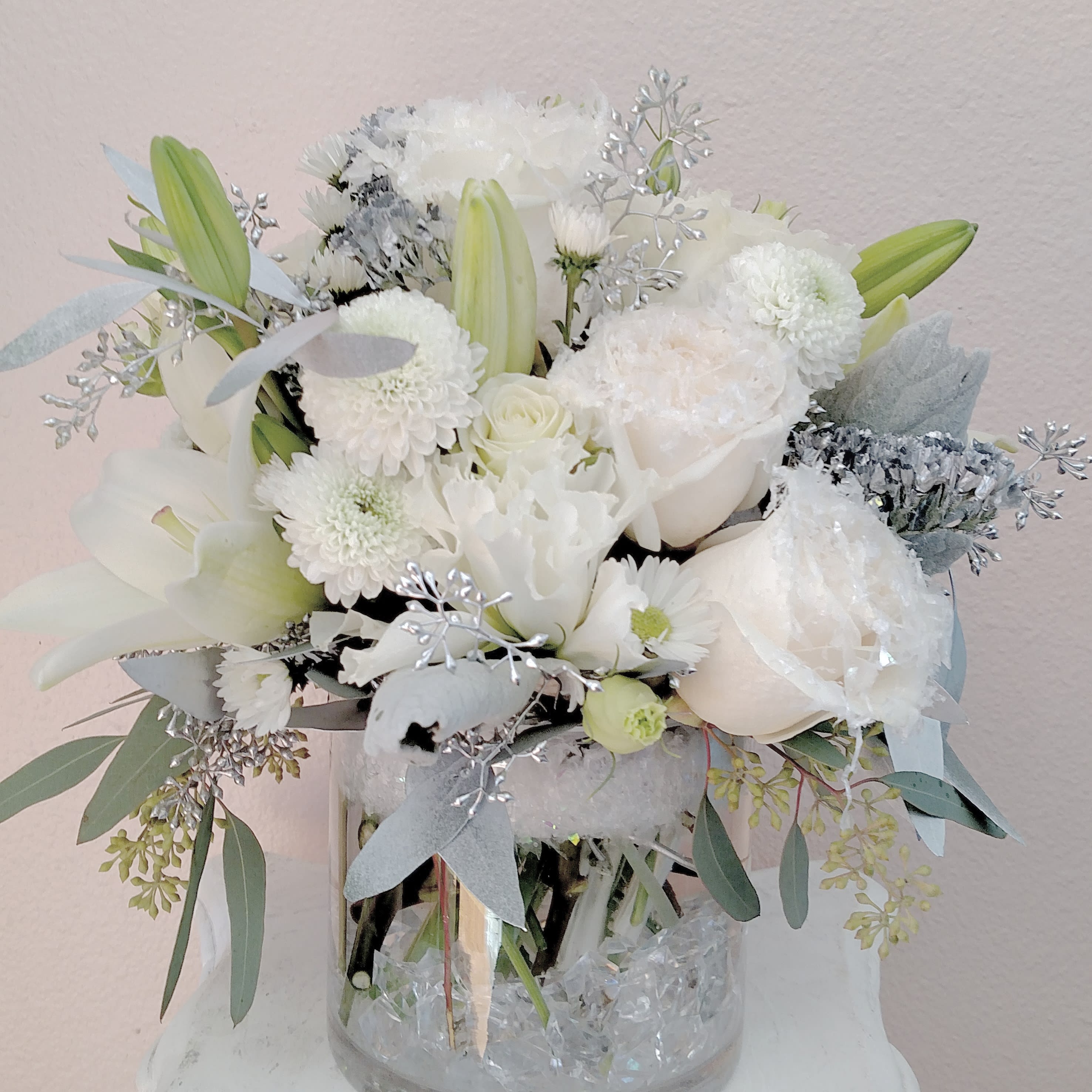 Winter Snow Rose Bouquet - Snowy white roses, lilies, lisianthus, silver eucalyptus and mixed greens come together in a glass cylinder vase to bring a sense calm amid the holiday hustle and bustle.