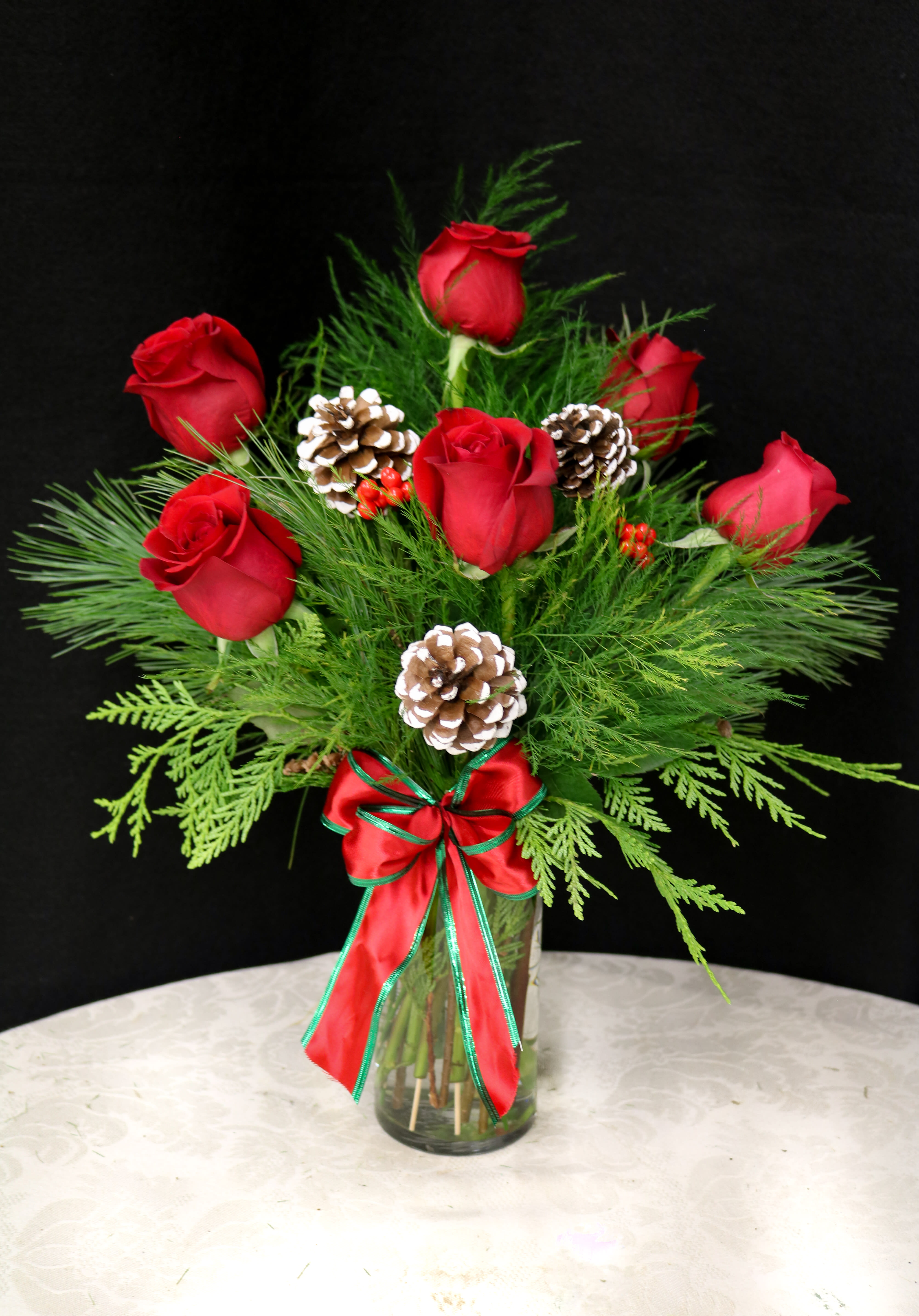 Holiday Roses - Half a dozen red roses accompanied by winter greens and pine cones with a festive bow