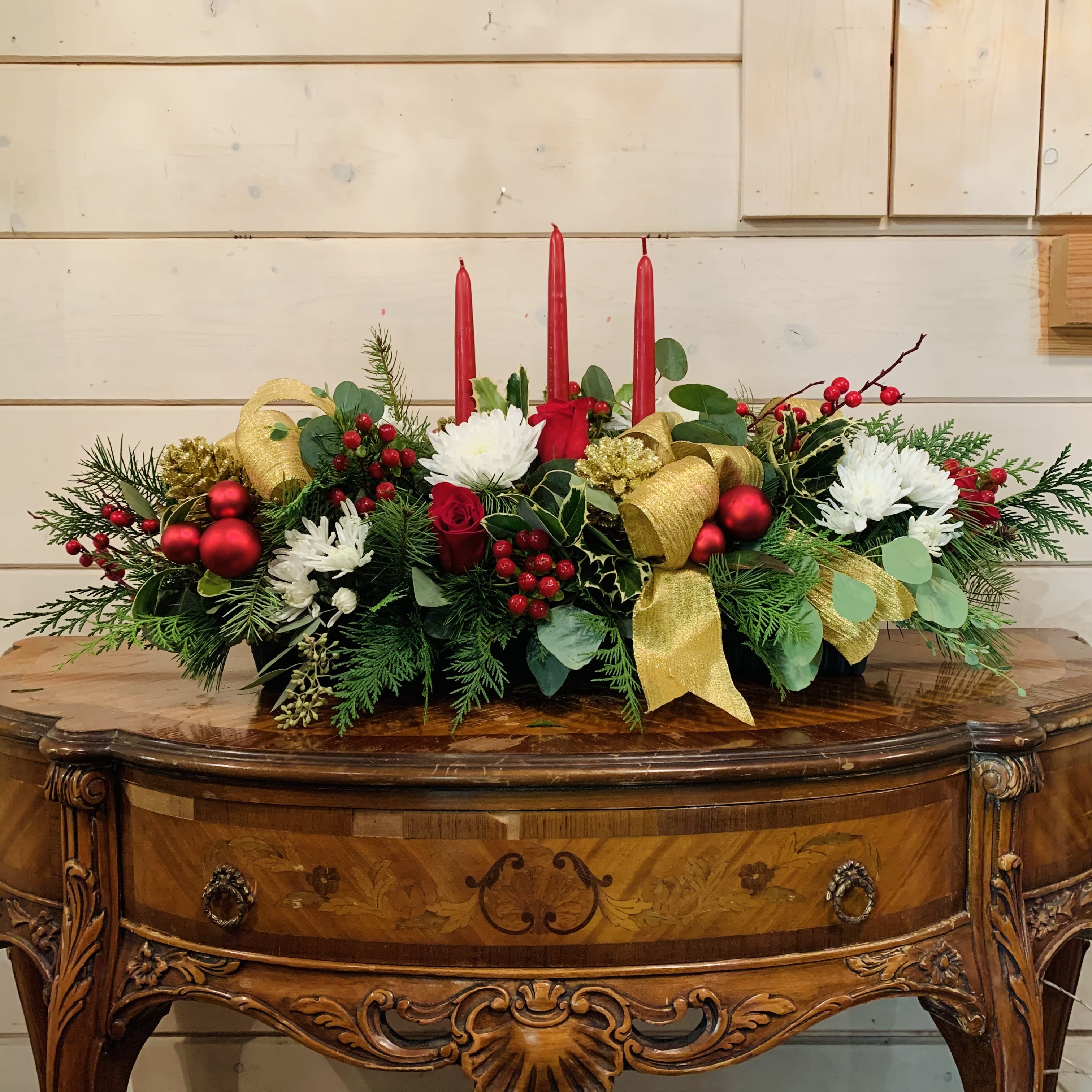 Riz's Favorite Centerpiece  - Red roses, white chrysanthemums, red hypericum berries arranged in a long tray with silk berry branches, large gold bows, gold glitter pinecones and red ornament balls. Comes with three burgundy candles. Approximately 30in long and 9in tall.  