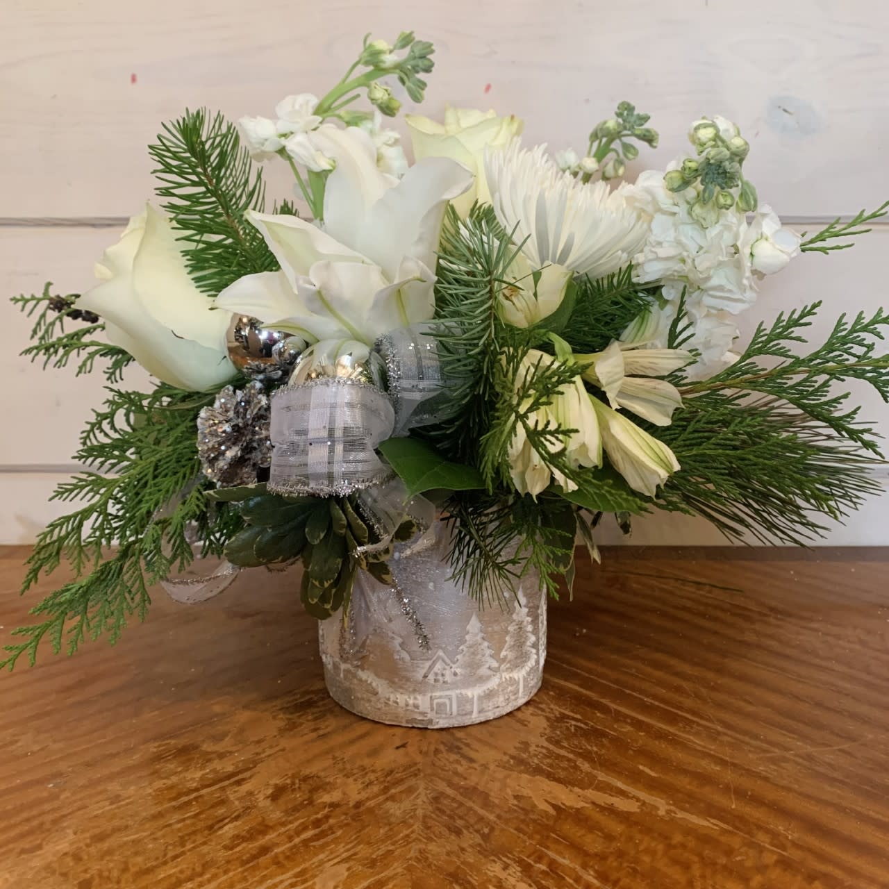 Silver Cityscape Bouquet  - All white flowers including an assortment of roses, lilies, stock, chrysanthemums and alstroemeria arranged in a silver pot embossed with quaint homes and trees. Winter evergreens, silver ornament balls, and glittered pinecones complete this festive arrangement. 