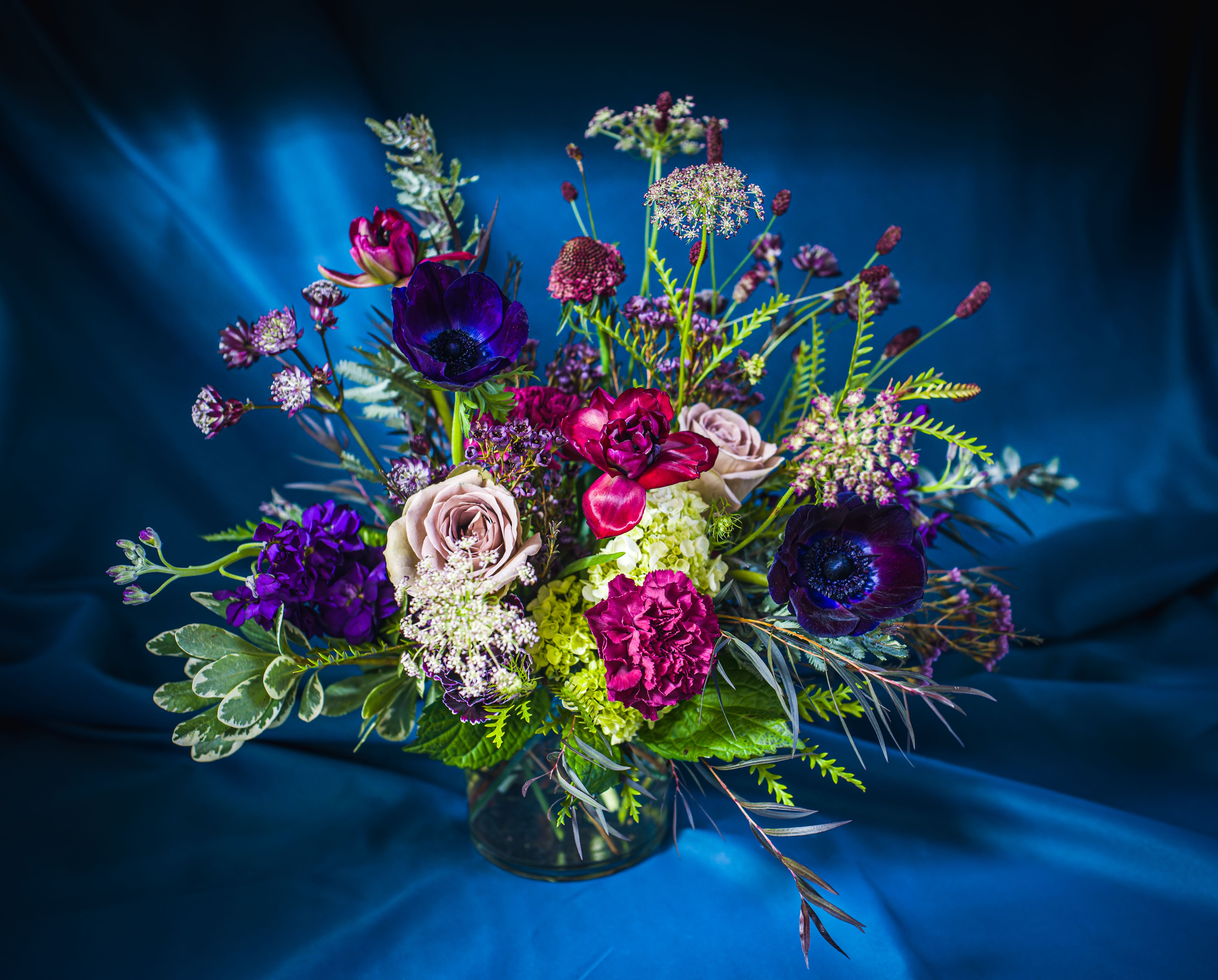 Designer’s Choice FIGGY PUDDING VASED ARRANGEMENT (Deep plums, greens, lavender, creams with hints of purple/lav/green) - A delectable collection of rich plums, deep burgundies, textural greens and tinted creams is sure to please the most sophisticated flower aficionado.  Both romantic and seasonal- pairs well with a cup of good cheer!