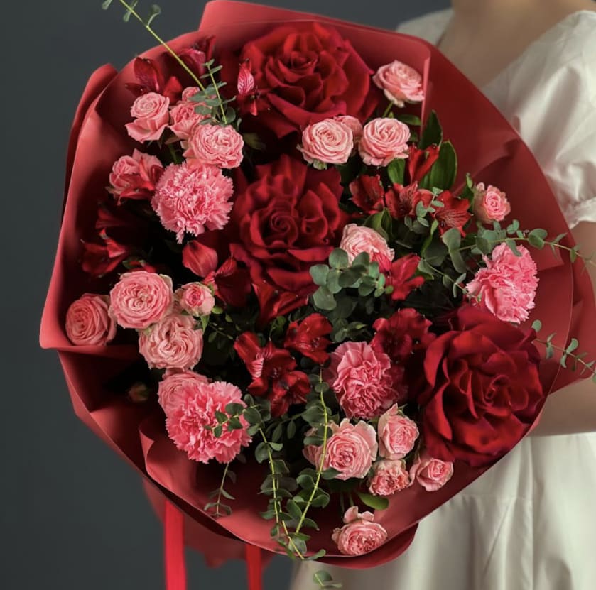 Love of blooms - This Bouquet is a dramatic fusion of romance and modern style, designed for someone who loves passion without restraint. Deep red roses and lush carnations set a rich, velvety foundation, while soft pink spray roses and blush tones add dimension, youthfulness, and charm. The interplay of color- from bold crimson to delicate pastel- creates a bouquet that feels both powerful and tender.  Accented with greenery for a fresh, contemporary silhouette, the arrangement is wrapped in rich paper that enhances its luxurious, couture aesthetic. Perfect for anniversaries, birthdays, romantic gestures, or a striking, elevated floral gift that makes a statement without saying a word.