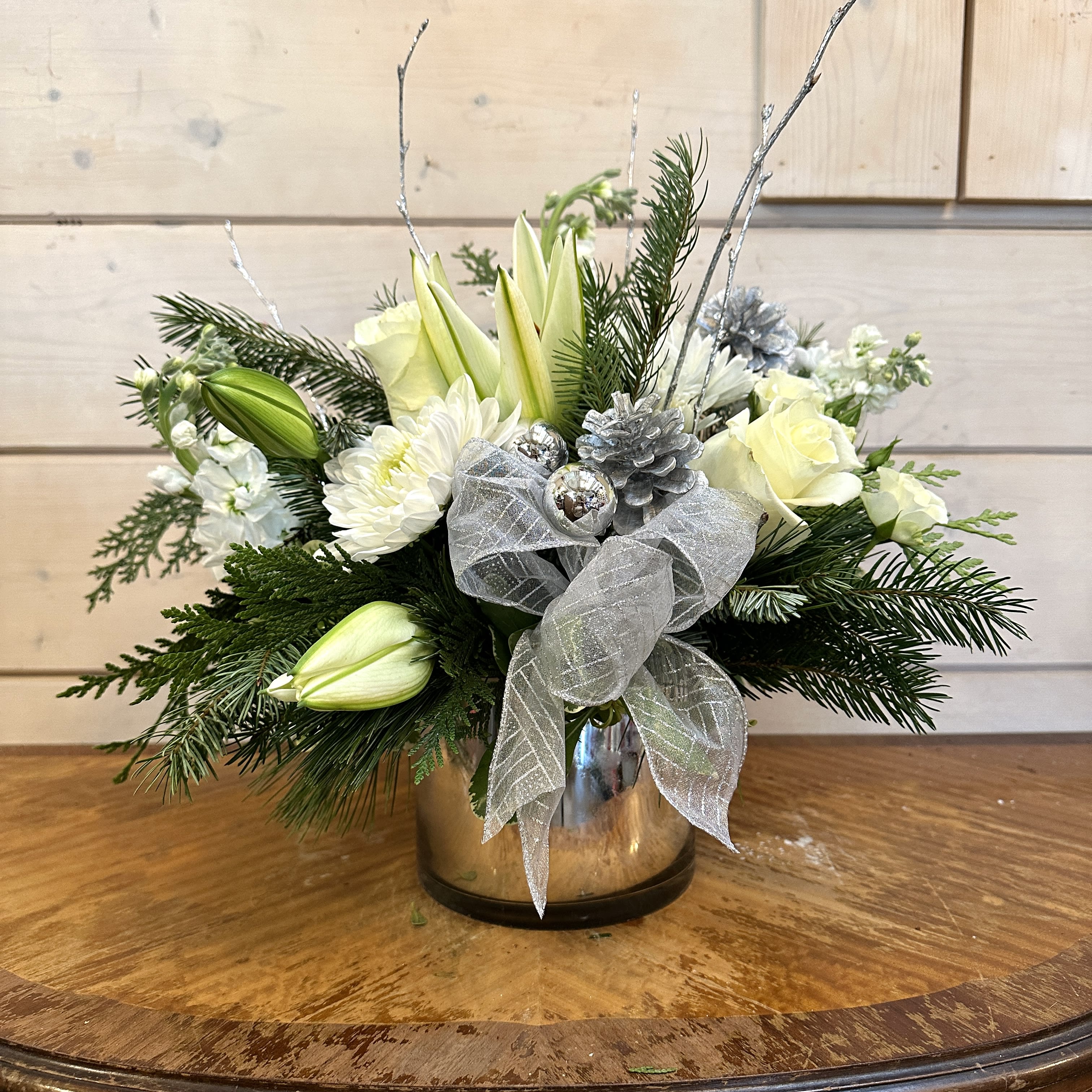 Winter White Bouquet  - All white arrangement includes roses, stock, chrysanthemums, and lilies arranged in a large silver gather . Includes silver glitter branches, bows and pinecones. Approximately 12in tall and 14in wide.  