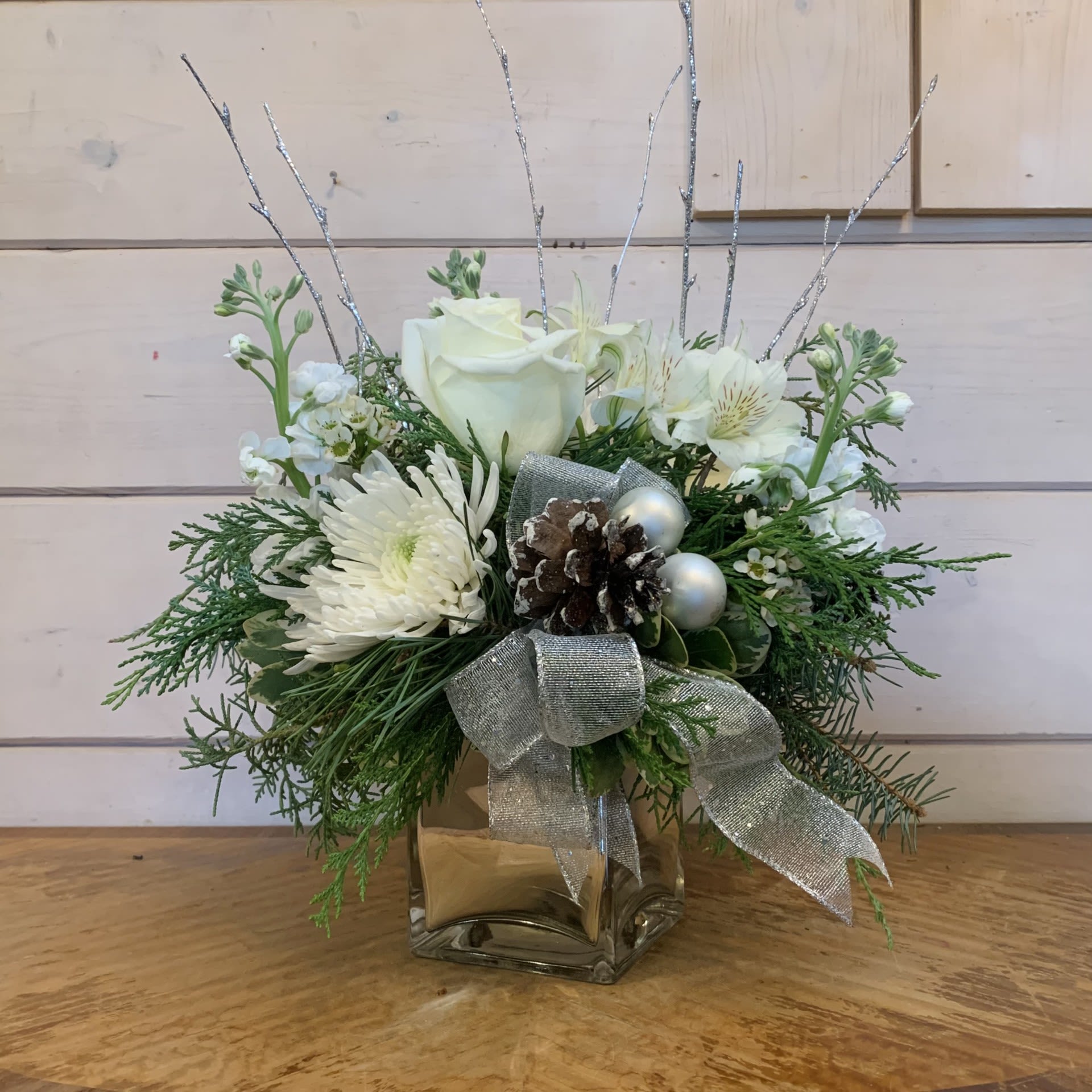 Simply Silver Bouquet  - An all white and silver arrangement with red roses, white chrysanthemums, white stock, and white alstroemeria arranged in a silver cube, with a silver bow, glitter pinecones, white ornament balls, glitter branches and seasonal white filler flower. Approximately 11&quot; tall and 10&quot; wide. 