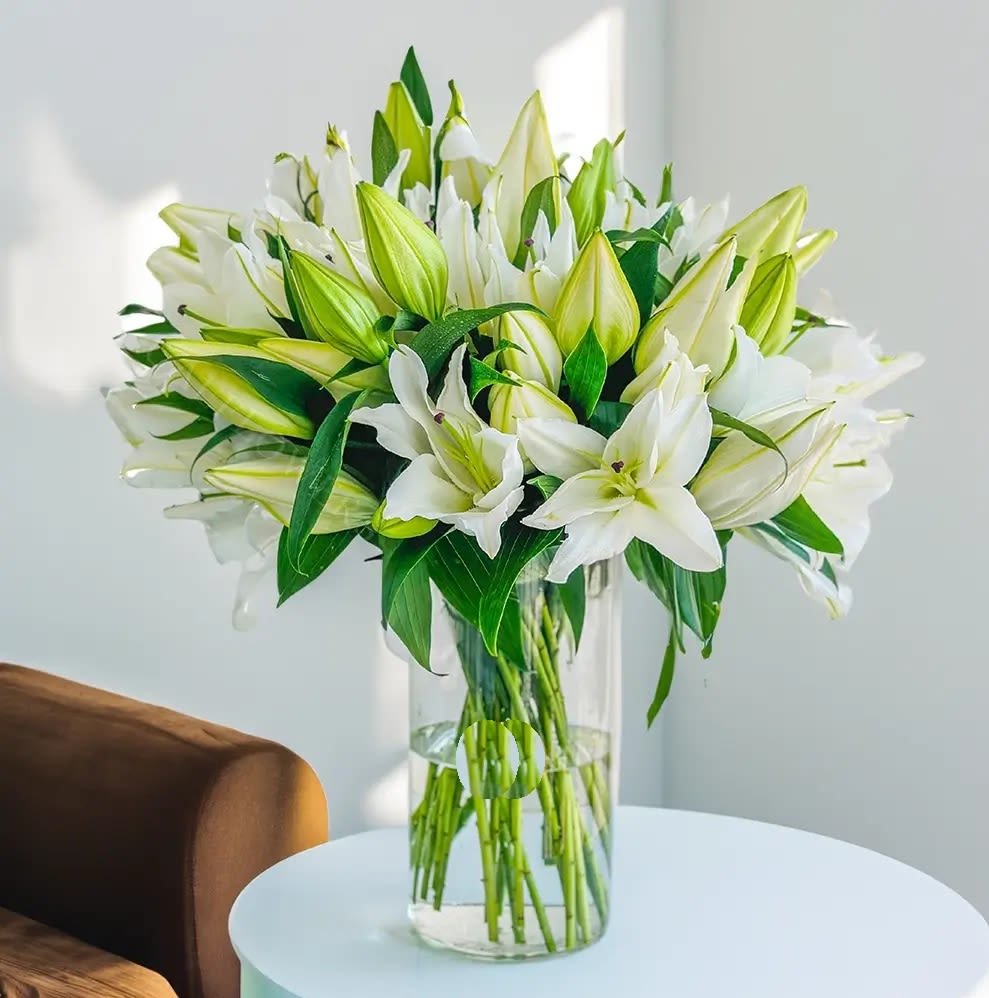  Elegant  Lilies  Arrangement   - This elegant arrangement features  white lilies accompanied by fresh green fillers, displayed in a sleek glass vase. The simplicity of the white lilies paired with the natural greenery creates a serene and timeless display, perfect for any occasion.