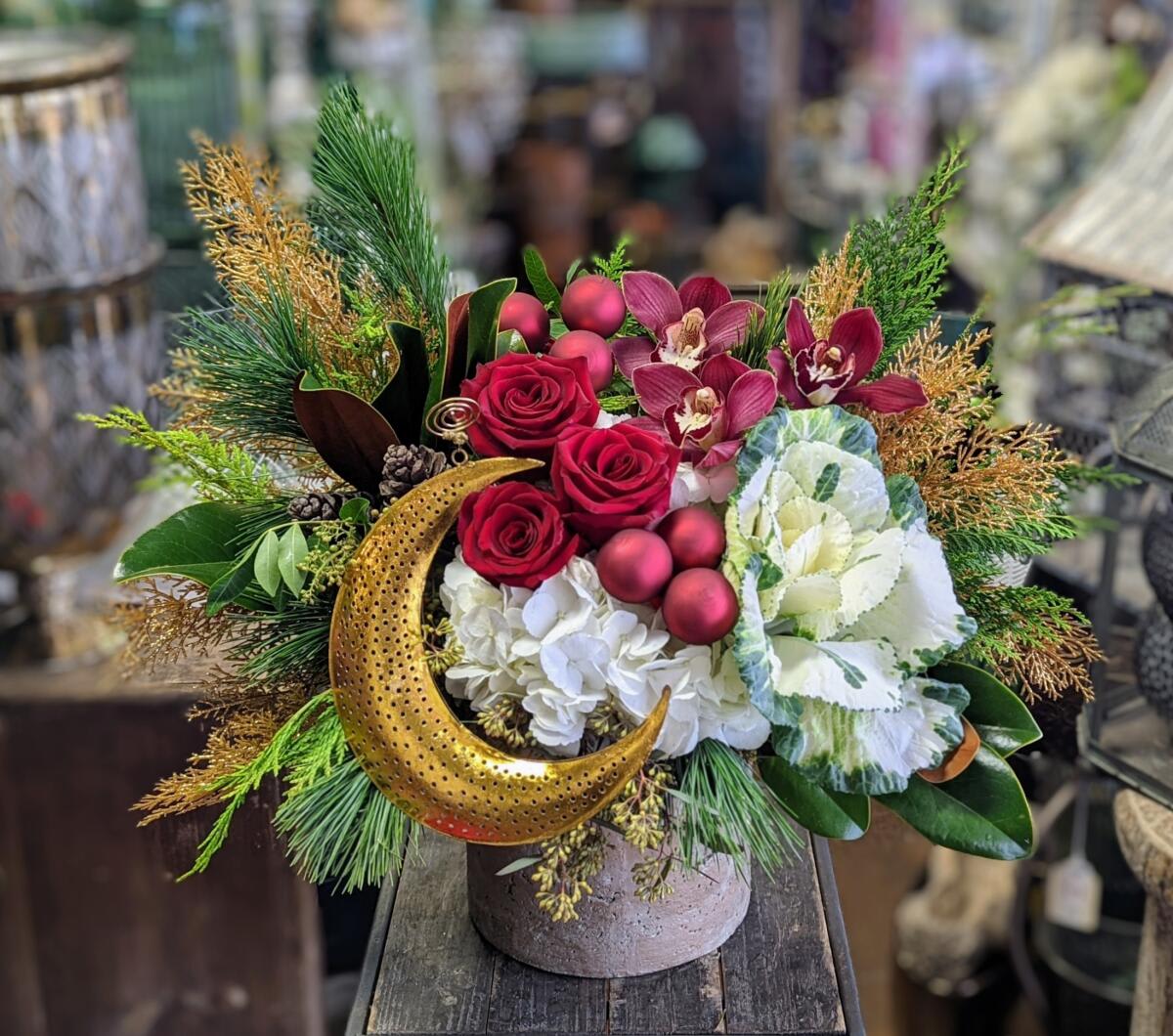 Zenith - Zenith – A Lunar Holiday Statement Piece Illuminate the season with Zenith, a luxurious celestial-inspired arrangement handcrafted by Windmill Floral Expressions in Las Vegas. This artistic holiday design blends rich winter textures with bold, vibrant florals—creating a show-stopping centerpiece that feels both mystical and modern.  Deep red roses and burgundy cymbidium orchids add dramatic, velvety color, while white hydrangea and ornamental cabbage bring soft winter brightness. Lush evergreens, golden cedar, pinecones, and magnolia foliage layer in that enchanting “enchanted forest” feel—perfect for elevating any holiday tablescape or gifting something truly unforgettable.  The star of Zenith is the sculpted golden crescent moon, glowing against a cluster of matte red holiday ornaments. This signature celestial touch makes the arrangement feel magical, moody, and unmistakably Windmill Floral.  Perfect for: • Holiday tables, winter parties, and seasonal décor • Unique luxury gifts in Las Vegas &amp; Henderson • Celestial, boho, and nature-inspired holiday themes • Clients seeking custom high-end floral art  Zenith brings together the magic of winter, the glow of the moon, and the artistry of premium florals—creating a piece that feels like the season’s brightest moment.