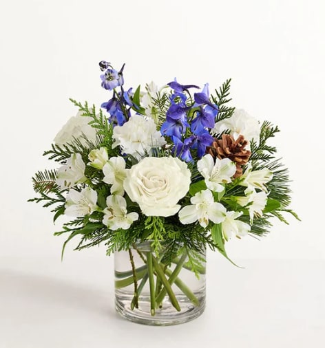 Winter Wishes - Inspired by winter’s cool blue &amp; white landscape, our delightful arrangement delivers warm wishes to the people you love. Hand-designed with a lush gathering of blooms, evergreens and rustic touches, it’s a thoughtful sentiment filled with the season’s natural beauty.