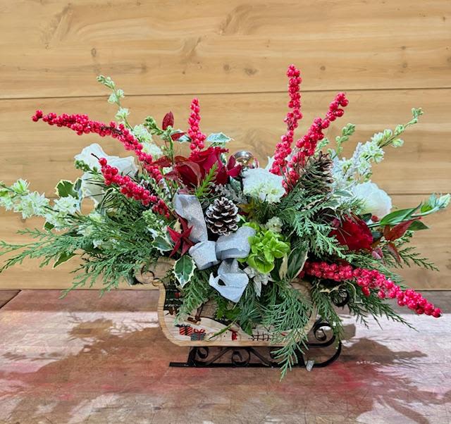 Sleigh ride - Come take a trip through the winter wonderland with this beautiful Sleigh Ride. This is arranged in a stunning  wood carved snowman sleigh featuring gorgeous red and white roses amongst other flowers in a bed of fresh Christmas greens. Sure to warm anybody's heart. 