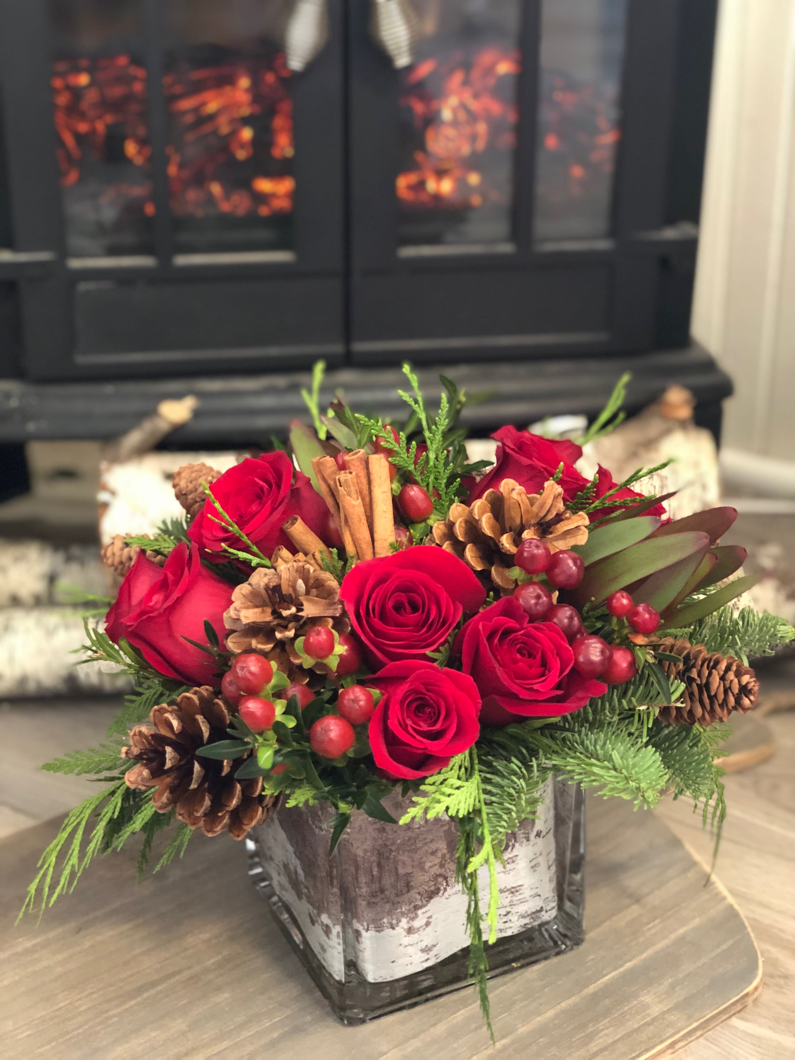 Christmas Cheer - Send holiday greetings with rich reds hues and seasonal textures like pinecones and evergreens. Exact flower selection may vary daily.  Shown approx. 10x10