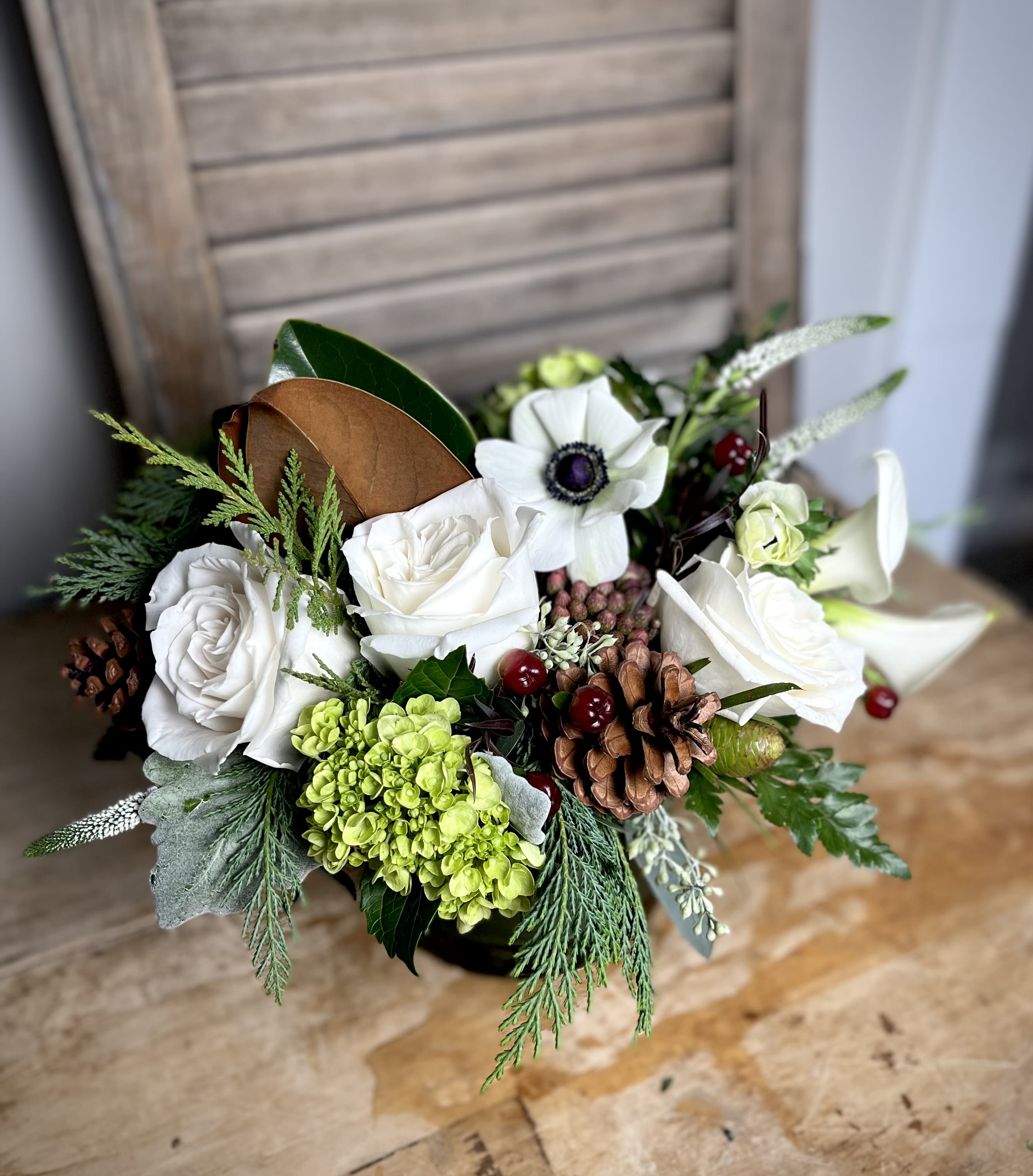 Winter Country Classic -  Elegant ivory roses with a backdrop of winter textures such a pinecones, berries and evergreens.  Deluxe version shown. 