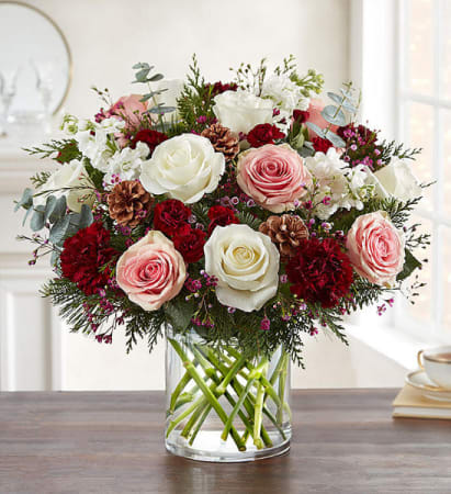 Frosted Rose Couture - A romantic twist on winter elegance, this premium bouquet showcases a lush blend of white and blush roses paired with rich burgundy carnations, winter greenery, and frosted eucalyptus. Accents of natural pinecones and red berries add a touch of seasonal luxury, while soft filler blooms create depth and movement throughout the design. Styled in a modern clear glass vase with clean, structured stems, this arrangement brings a sophisticated balance of freshness, warmth, and holiday charm—perfect for gifting or elevating any seasonal space.