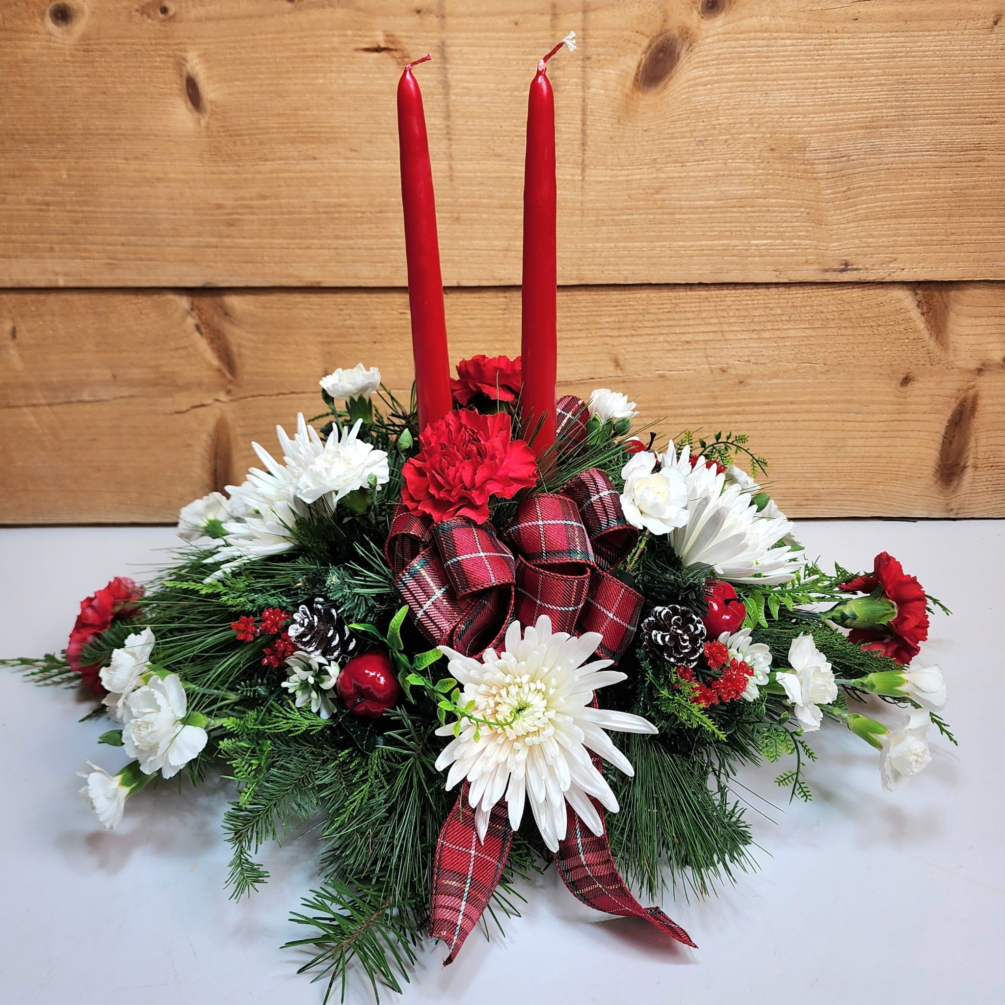 Merry &amp; Bright Centerpiece - Our Merry &amp; Bright Centerpiece is sure to light up your life this season! Our centerpiece has two red tapered candles, and also includes red carnations and white mums to get you in the holiday spirit! This arrangement would look perfect on your dinner table for holiday dinners, or makes the best hosting gift for someone you want to spread cheer to this season!  Dimensions approx. L 18” x H 15”