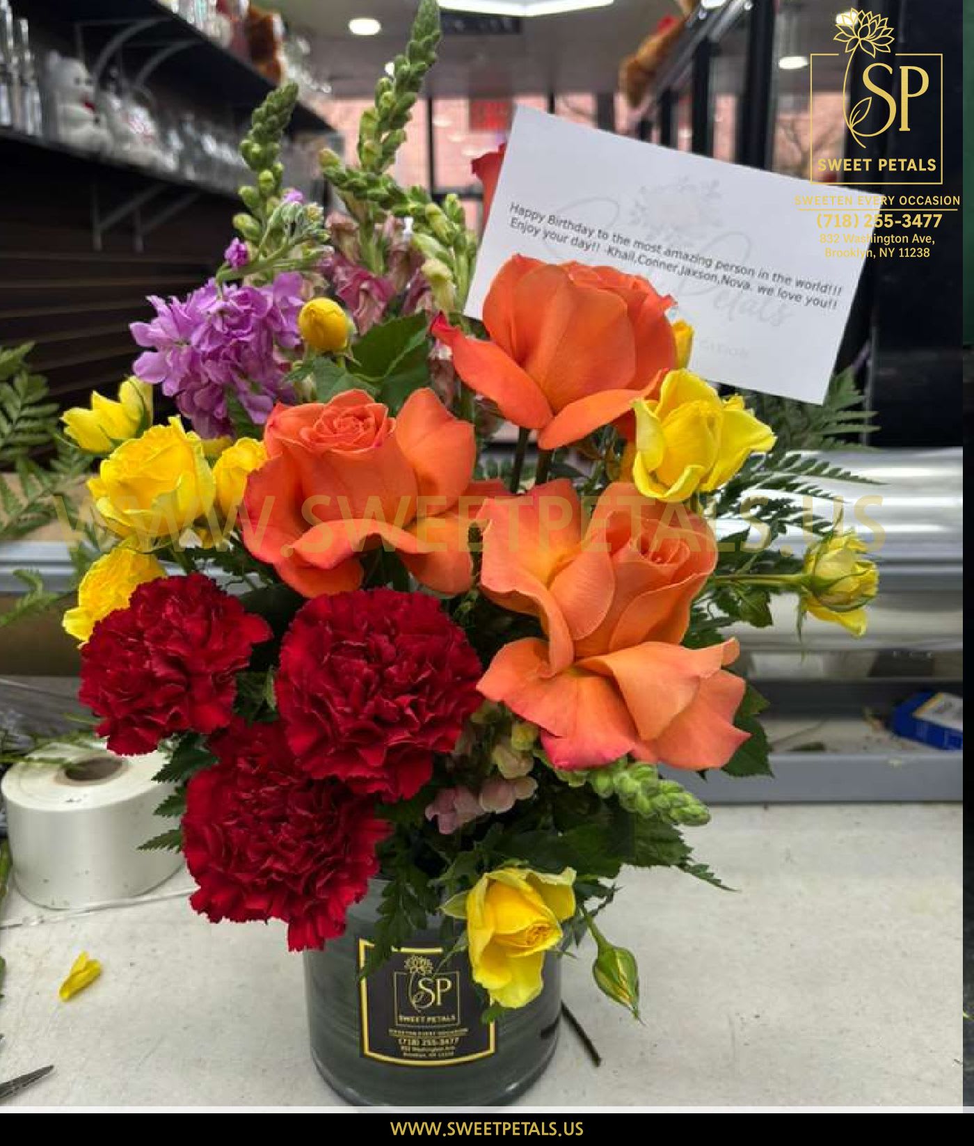 Sunset Radiance Vase Arrangement by SweetPetals - The Sunset Radiance Vase Arrangement by SweetPetals is a stunning burst of warm, bold, and joyful colors—perfect for brightening anyone’s day. This vibrant design features glowing orange roses, bright yellow spray roses, rich red carnations, soft pink snaps, and touches of purple florals, all enhanced with lush greenery for a full, luxurious finish.  Hand-arranged in the signature SweetPetals premium vase, this bouquet captures the beauty of a sunset, symbolizing warmth, celebration, and happiness. Ideal for birthdays, congratulations, thank-you gifts, anniversaries, or any special occasion that calls for cheer and positivity.  Every stem is carefully selected by SweetPetals florists to ensure unmatched freshness, vivid color, and long-lasting enjoyment. This lively arrangement is designed to sweeten every moment.   SweetPetals – Sweeten Every Occasion. 