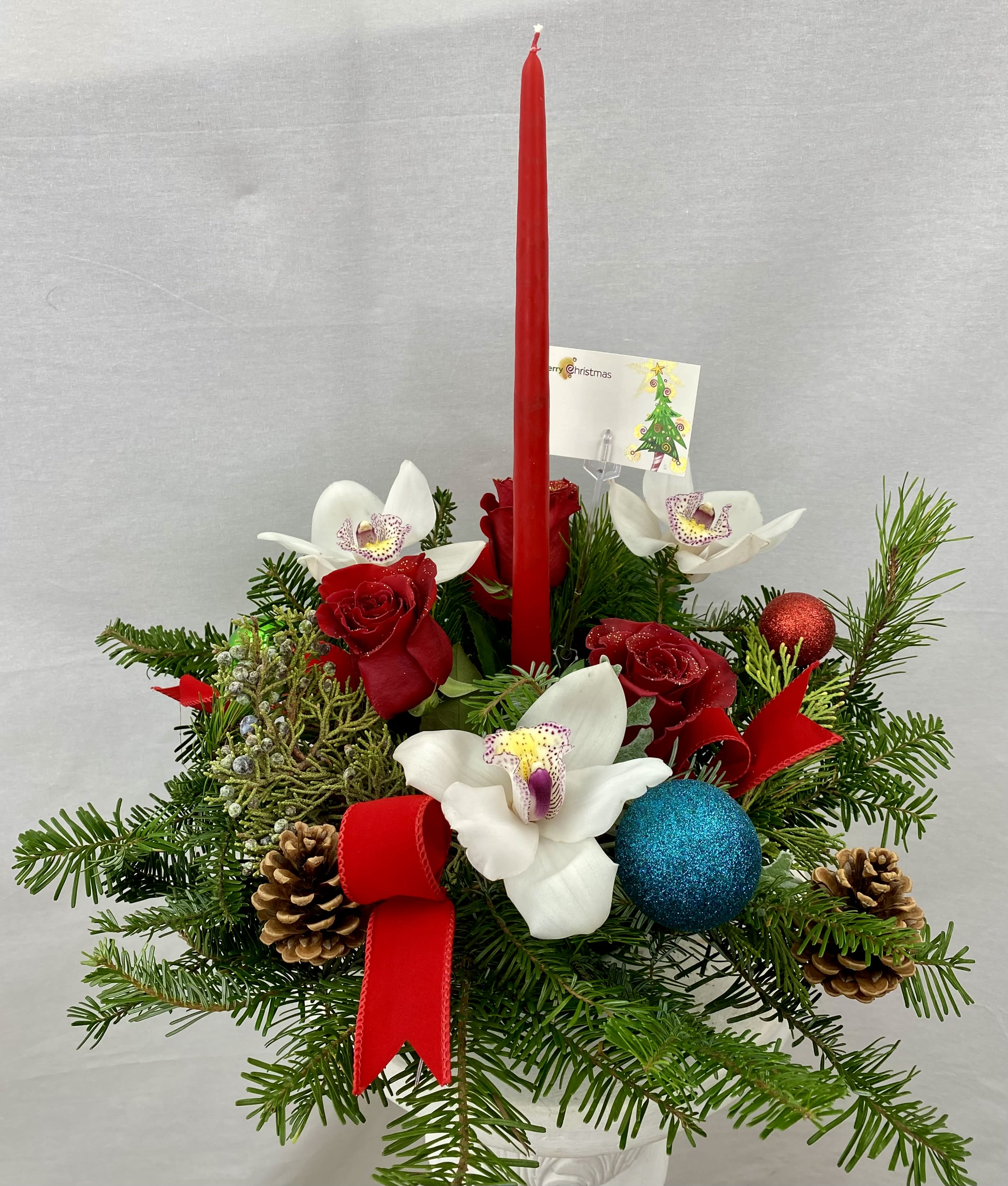 A Merry Christmas - A sweet round centerpiece with a long red candle for a jolly Christmas. A great holiday gesture featuring a mix of roses, orchids, ornaments, and fresh winter evergreens. 