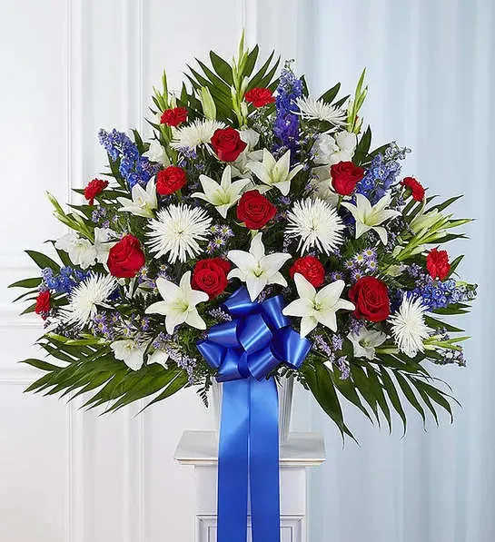  Red, White and Blue Standing Basket - The love they showed for their country is as deep as the love felt by those mourning their loss. Meticulously crafted by our expert florists to honor a proud veteran who has passed away, our majestic standing basket arrangement is filled with lush blooms in patriotic red, white and blue, creating a fitting final tribute for the funeral services.