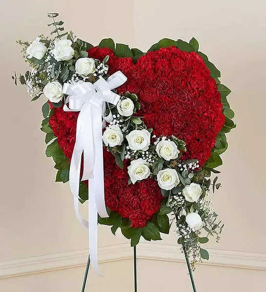 Floral Heart Tribute Red with White Roses - Honor a loved one with a special tribute. Our heart-shaped standing arrangement of fresh red carnations, accented by a cascading sash of white roses adorned with a white satin ribbon, will help you elegantly express your sincere devotion and sympathy.Arrangement of red carnations, white roses, gypsophila, spiral and seeded eucalyptus, salal and variegated pittosporum; accented with a white satin ribbon