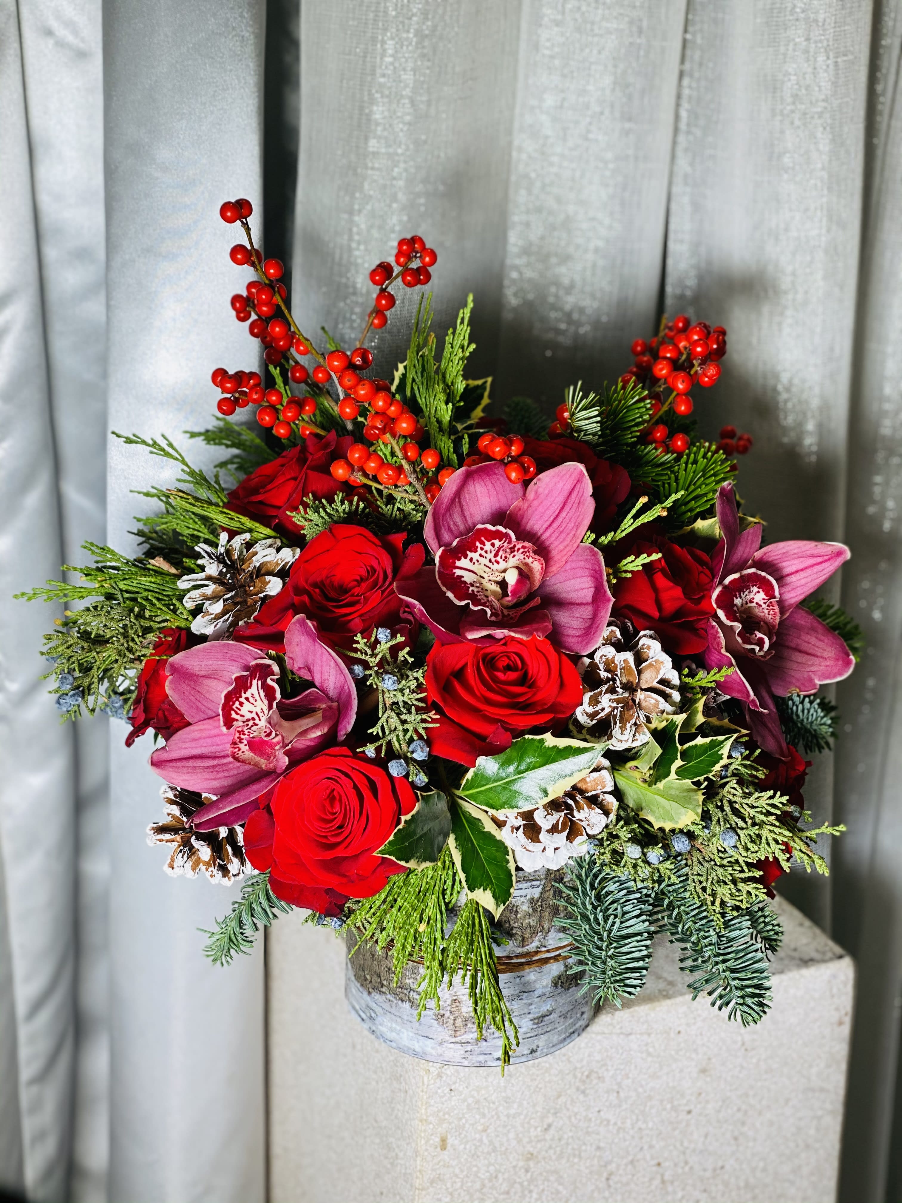 Rudolph - This adorable holiday themed arrangements has ilex berries, winter cymbidium orchids, pine cones, winter greens, and holiday red roses in a beautiful rustic themed container!