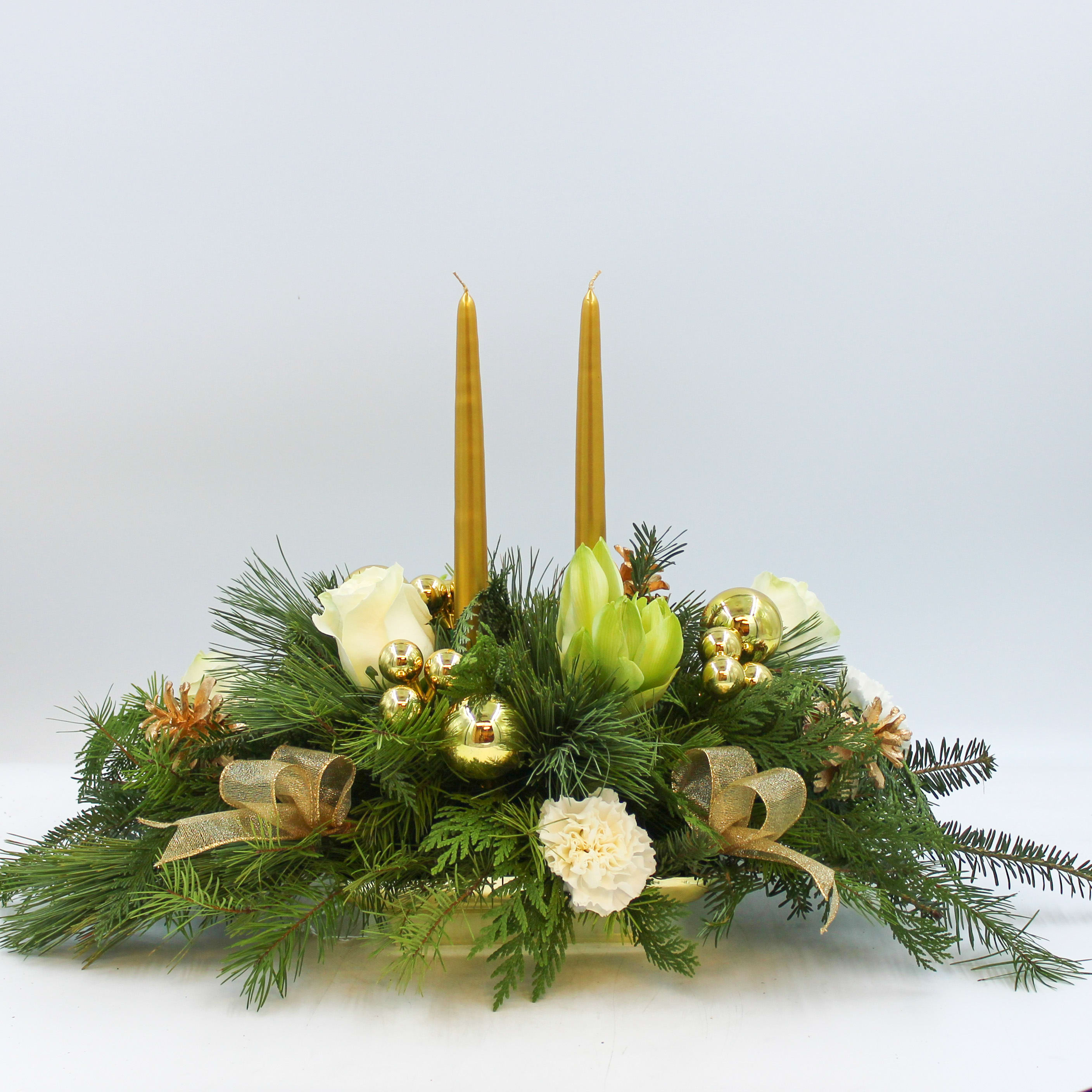 Vixen - Vixen is a gold and white traditional Christmas Centerpiece with White Amaryllis, White Roses, White Carnations, Gold Ornaments, Gold Ribbon and Gold Candles in a bed of mixed evergreens.