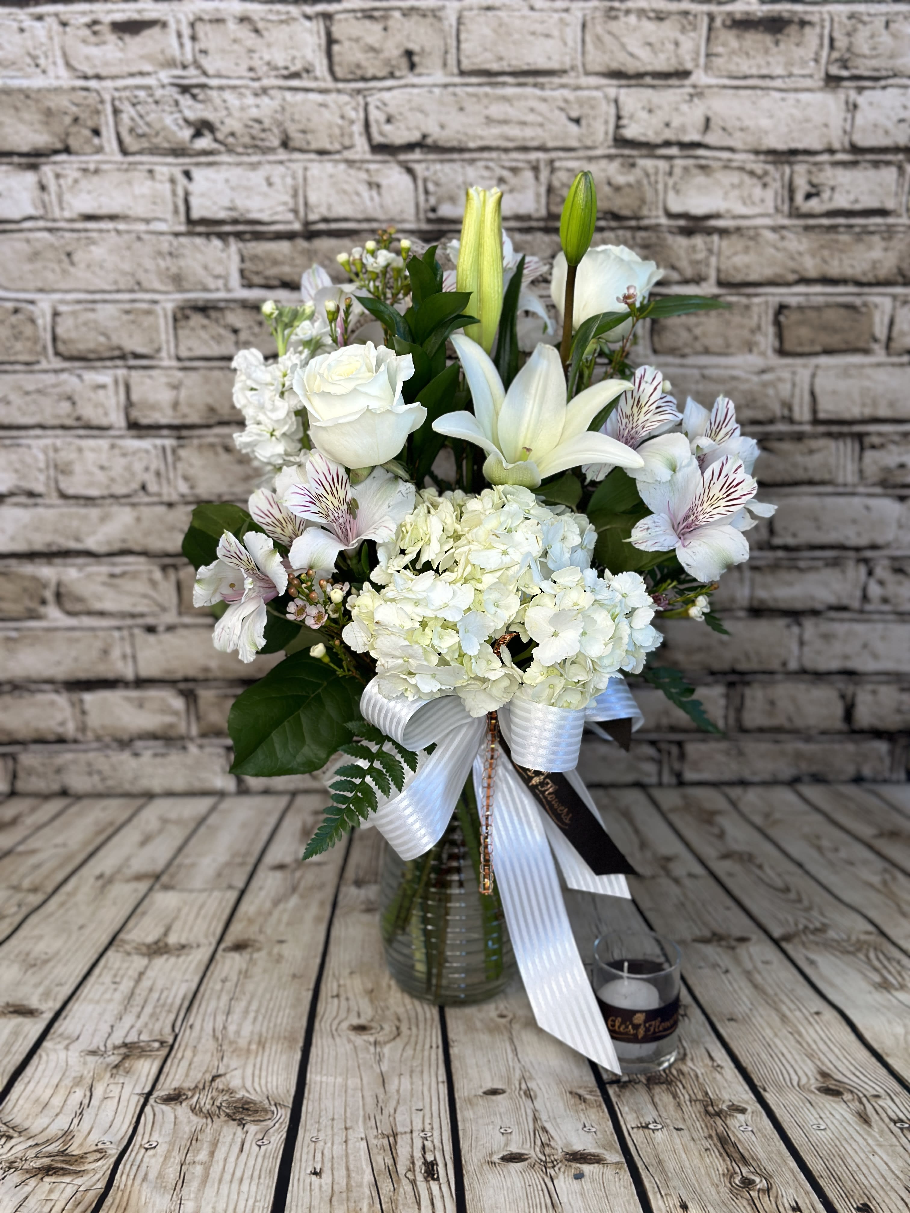 Serene White - Sympathy Arrangement - As peaceful and beautiful as a starry night, this pure white funeral bouquet is a touching way to remember a truly special person. Send this classic arrangement to comfort the newly bereaved at the funeral. Fresh white flowers are accompanied by lush greenery and accents to create a stunning bouquet of remembrance.    The designs we create are custom and the blooms and containers will vary. We use the freshest product available to create the perfect floral combination for the recipient! If you have any special requests, please add those in the "special instructions" portion of your order to help us dial in your vision. Otherwise, our skilled designers, Brett &amp; Sara, will take it from here!   *Please note that the photos are examples only – floral selection and containers will vary.*  Standard Size is an excellent option for a kitchen island. Approximate. Dimensions: ~20”H x 12”W  Deluxe Size is a great and showy, grand size for a larger kitchen table. Approximate. Dimensions: ~25"H x 18"W  Premium Size is an extravagant and luxurious display for a funeral service or celebration. Approximate Dimensions: ~30"H x 22"W  