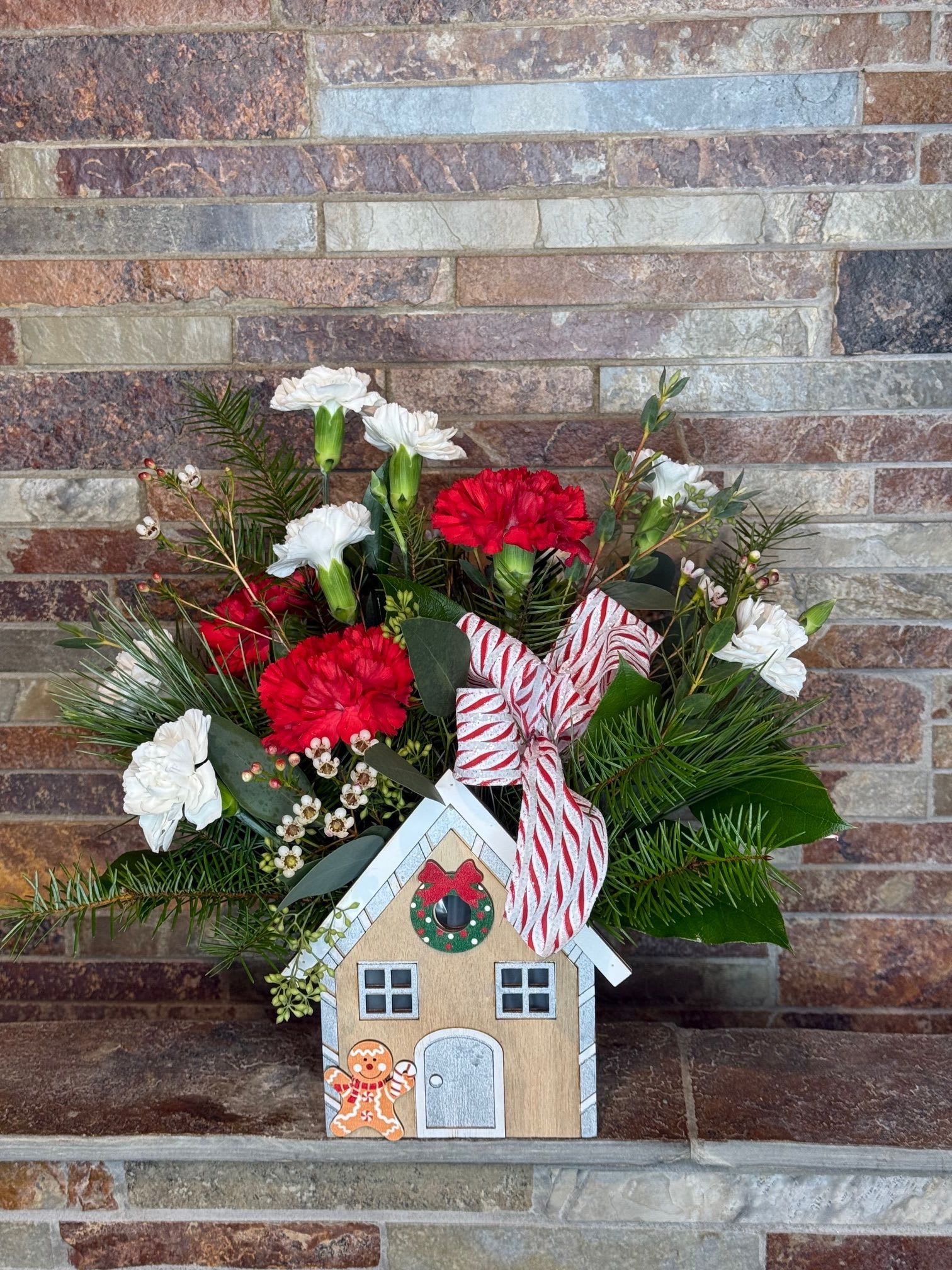 Gingerbread Dream - A super cute wooden box with a gingerbread house front, is filled with our longest lasting option - carnations! Standard and mini carns in red and white with seasonal greens will be the perfect cozy choice for the holiday!