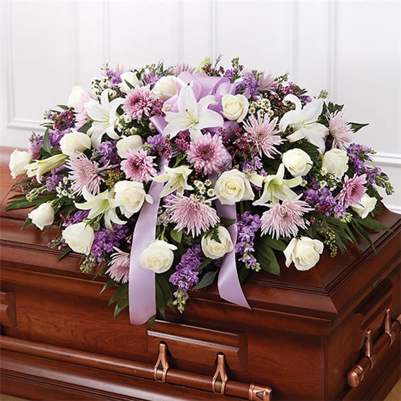 Lavender and White Half Casket Spray - Soft, graceful, and full of comfort, this beautiful casket spray features a calming blend of lavender, blush, and creamy white blooms. Designed with white roses, elegant white lilies, lavender cushion mums/spider mums, and rich purple accents (such as statice), this tribute is finished with a lavender satin ribbon and fresh greenery for a serene, classic presentation.
